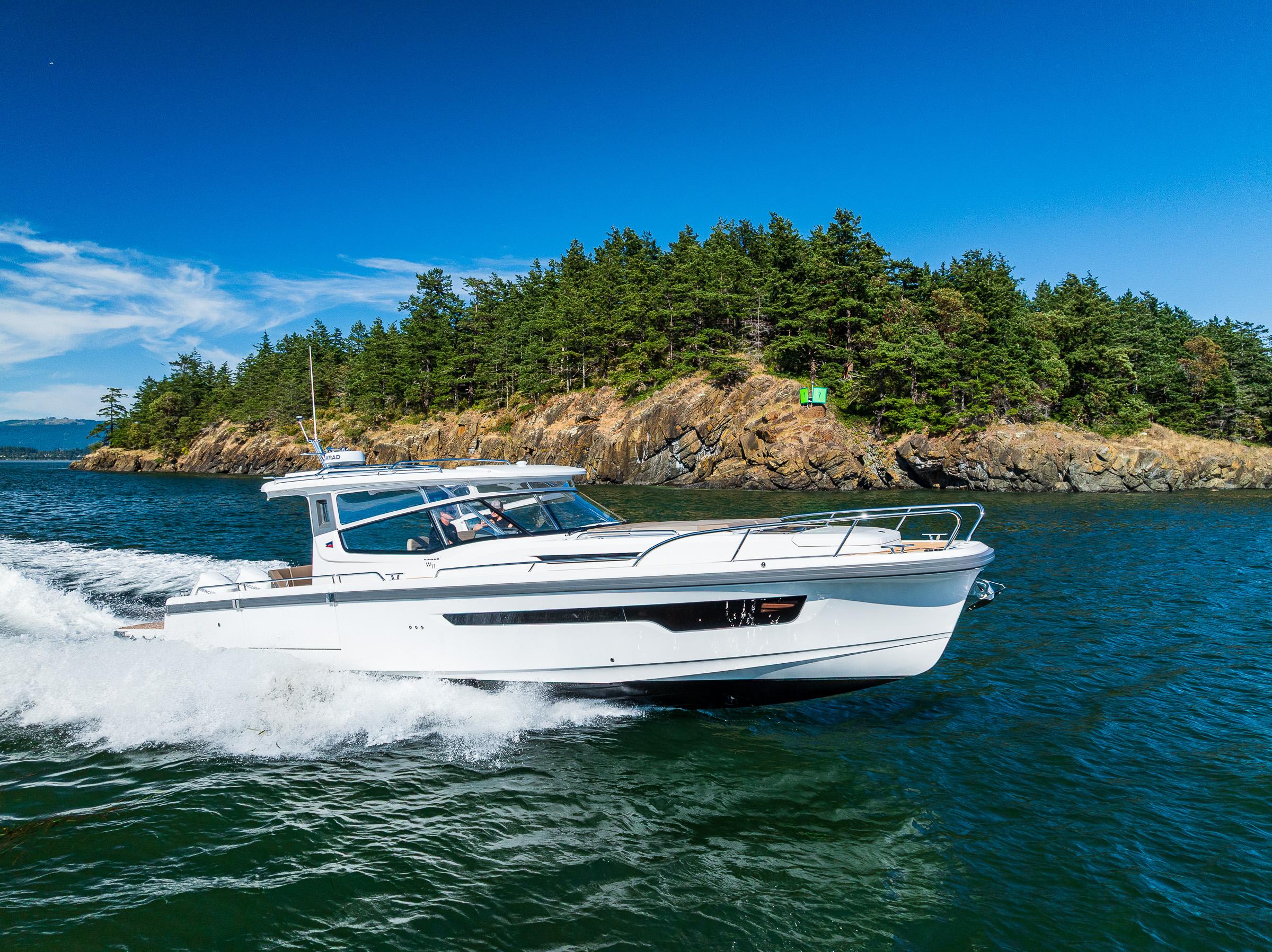 Nimbus W11 2025 boat cruising near a forested island under a clear blue sky.