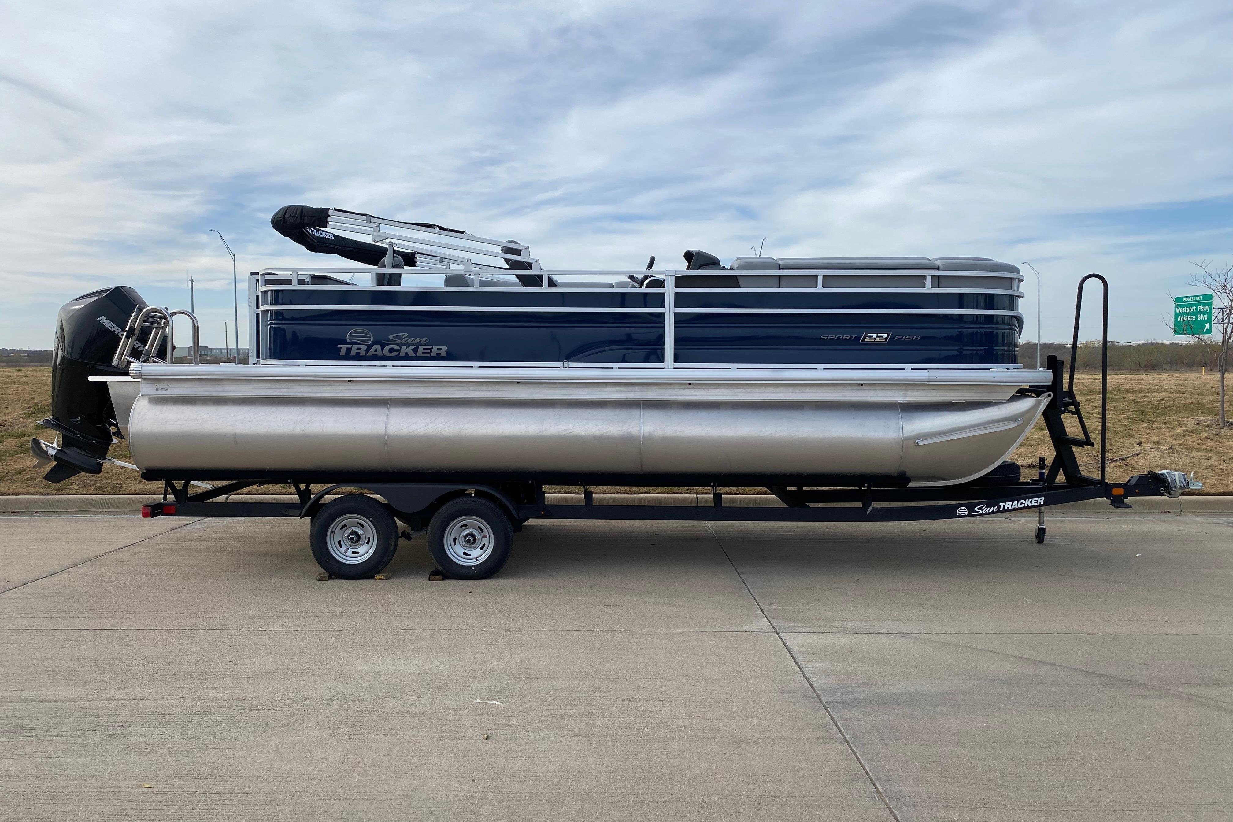 2026 Sun Tracker SportFish 22 XP3 pontoon boat on trailer, parked on roadside.