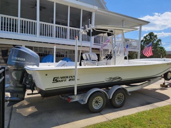 2011 Carolina Skiff 258 DLV boat on trailer, parked near a house with American flag.