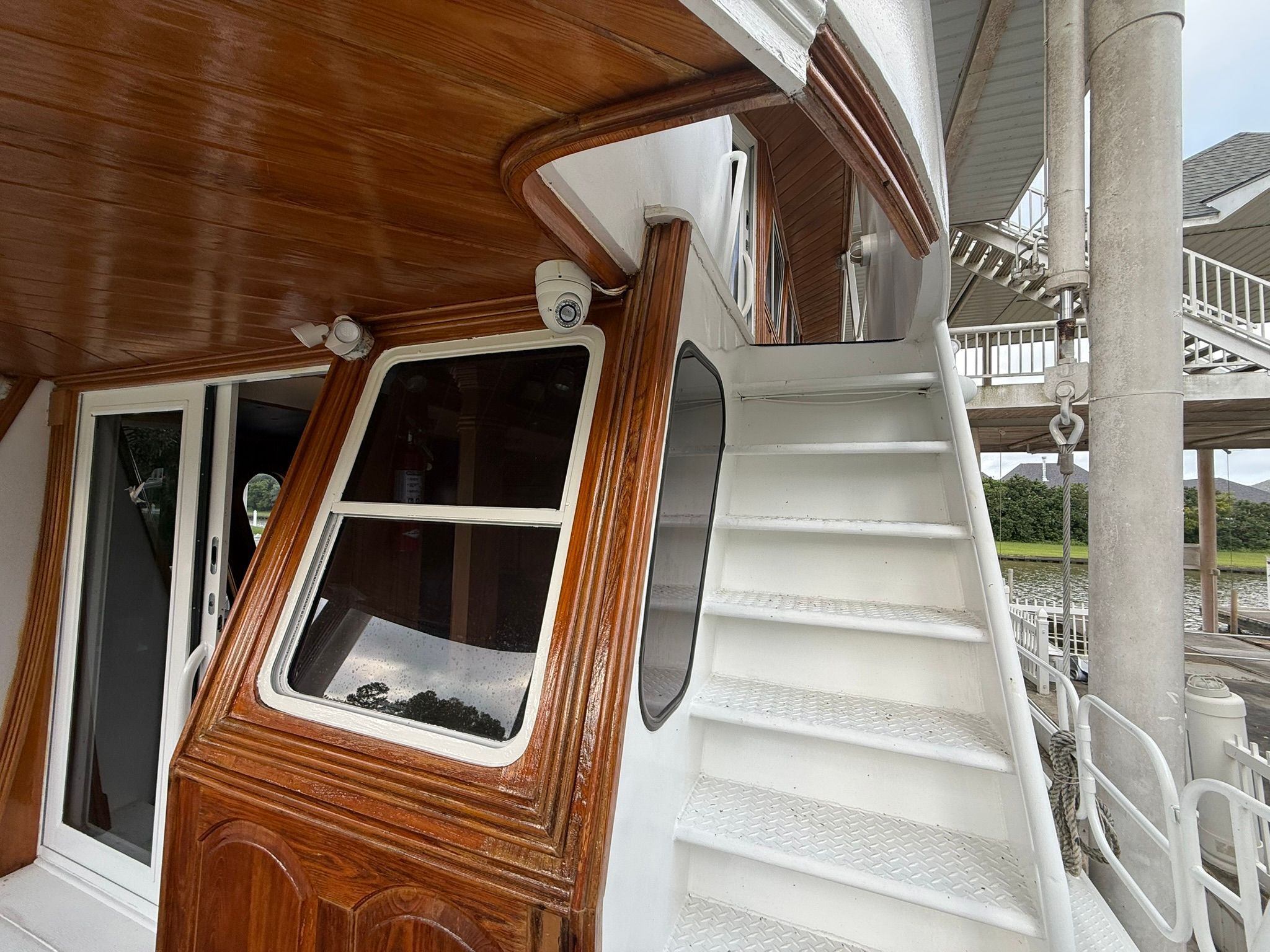 Wood-paneled boat with white stairs and windows, docked at a pier.
