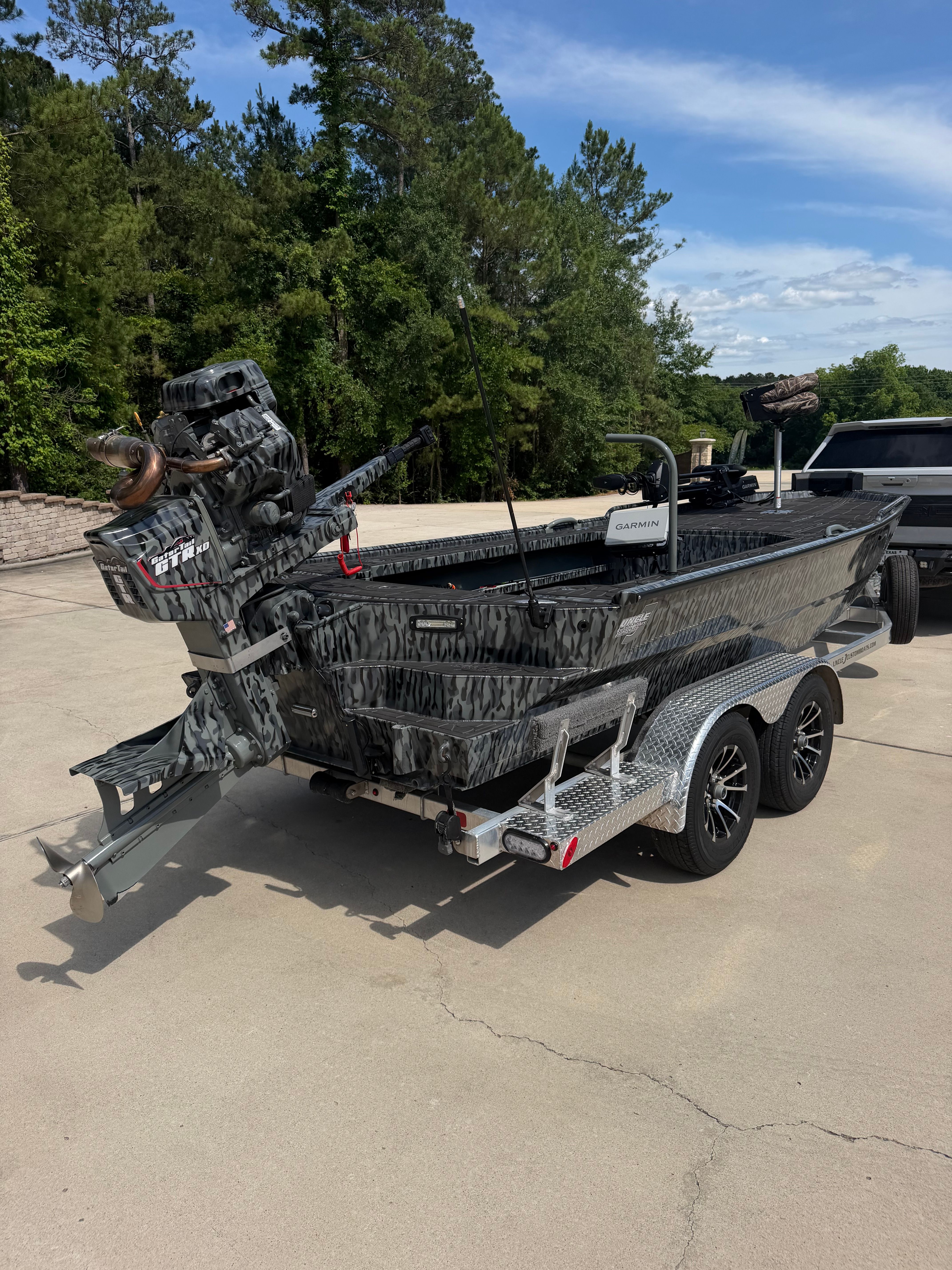 A camouflaged aluminum boat on a trailer, ready for transport.
