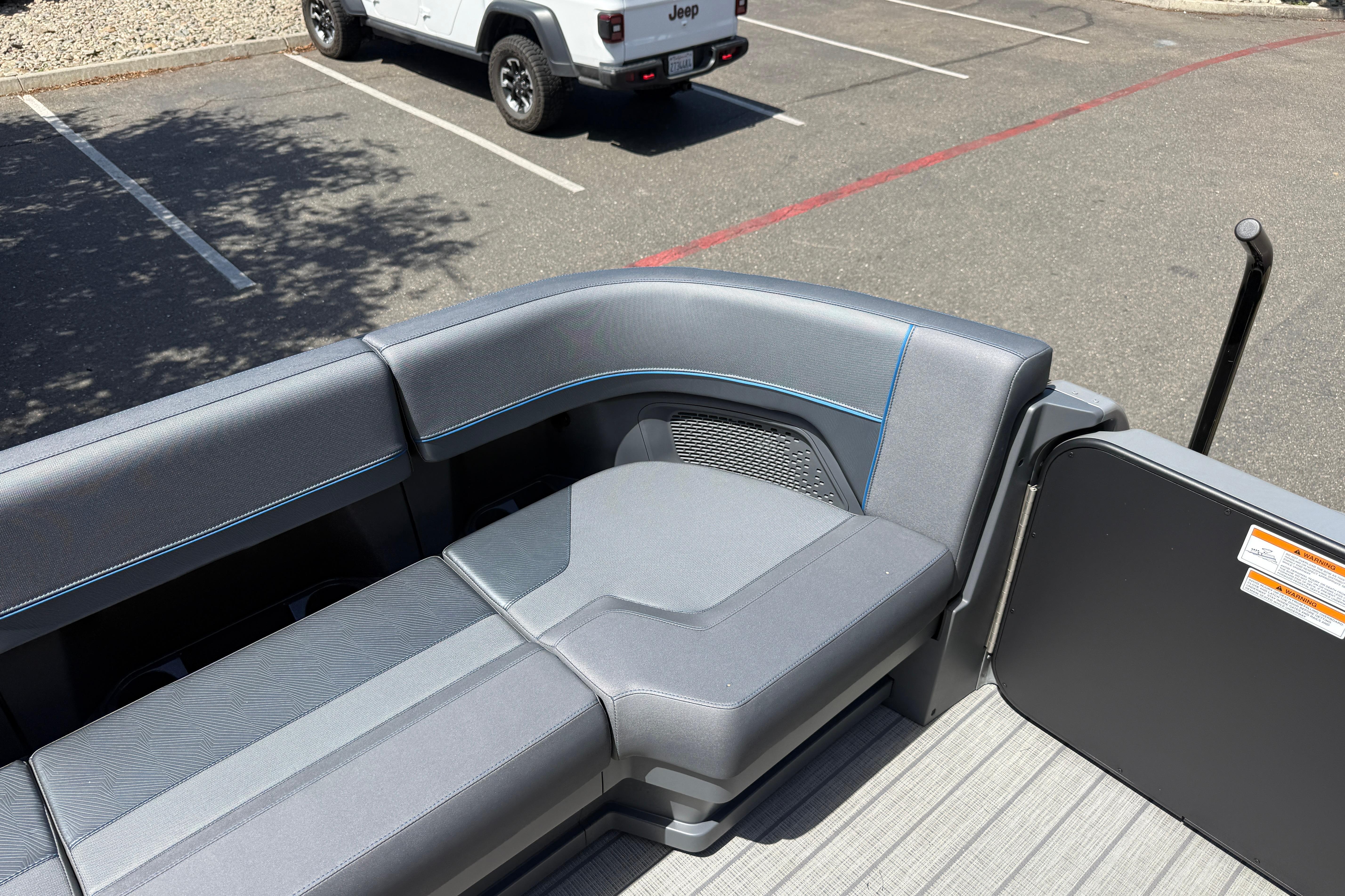 Luxurious seating on 2025 Manitou Explore Dual Engine pontoon boat in a parking lot.