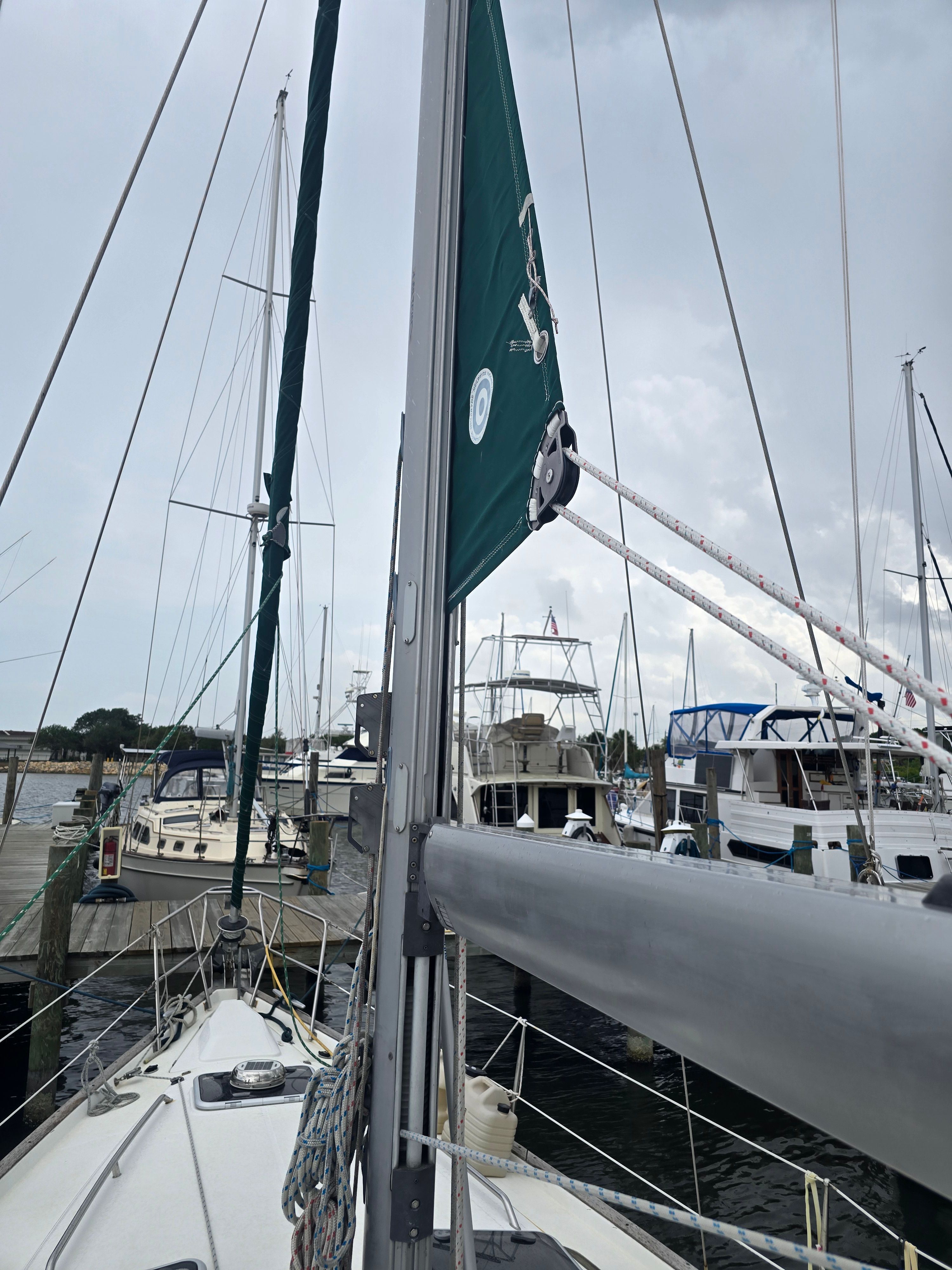 A sailboat is docked in a marina, surrounded by other boats. The mast and sail are visible.