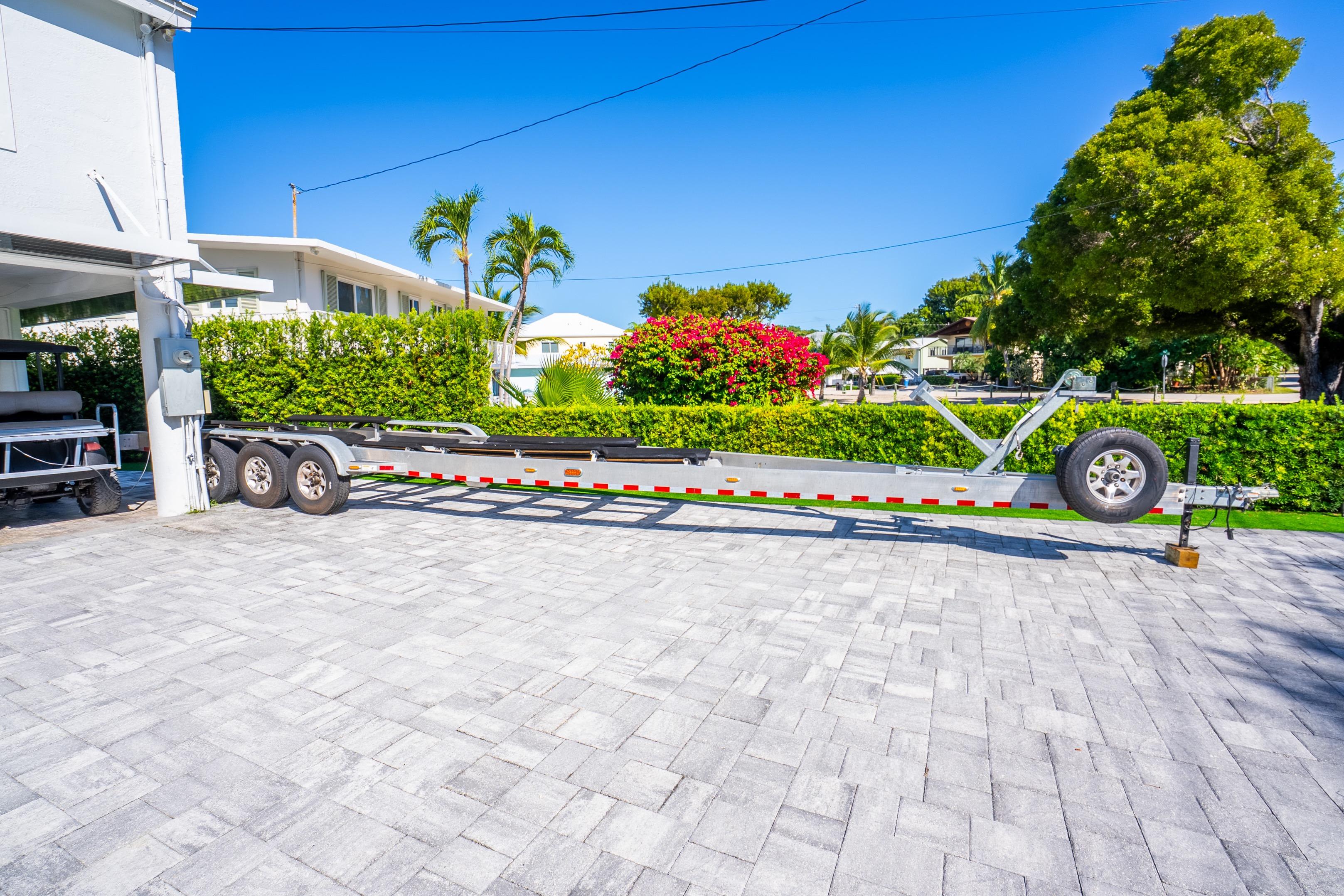 Trailer for 2016 Yellowfin 36 Offshore boat on paved driveway, surrounded by greenery.