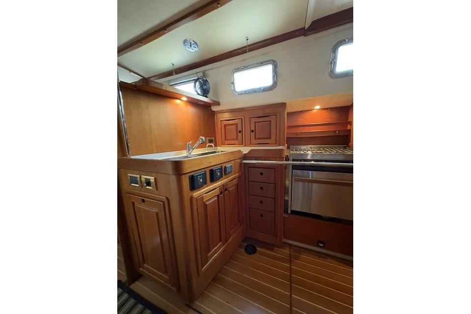 Wooden yacht kitchen interior with sink, stove, and cabinets in a 2002 Saga 43 model.