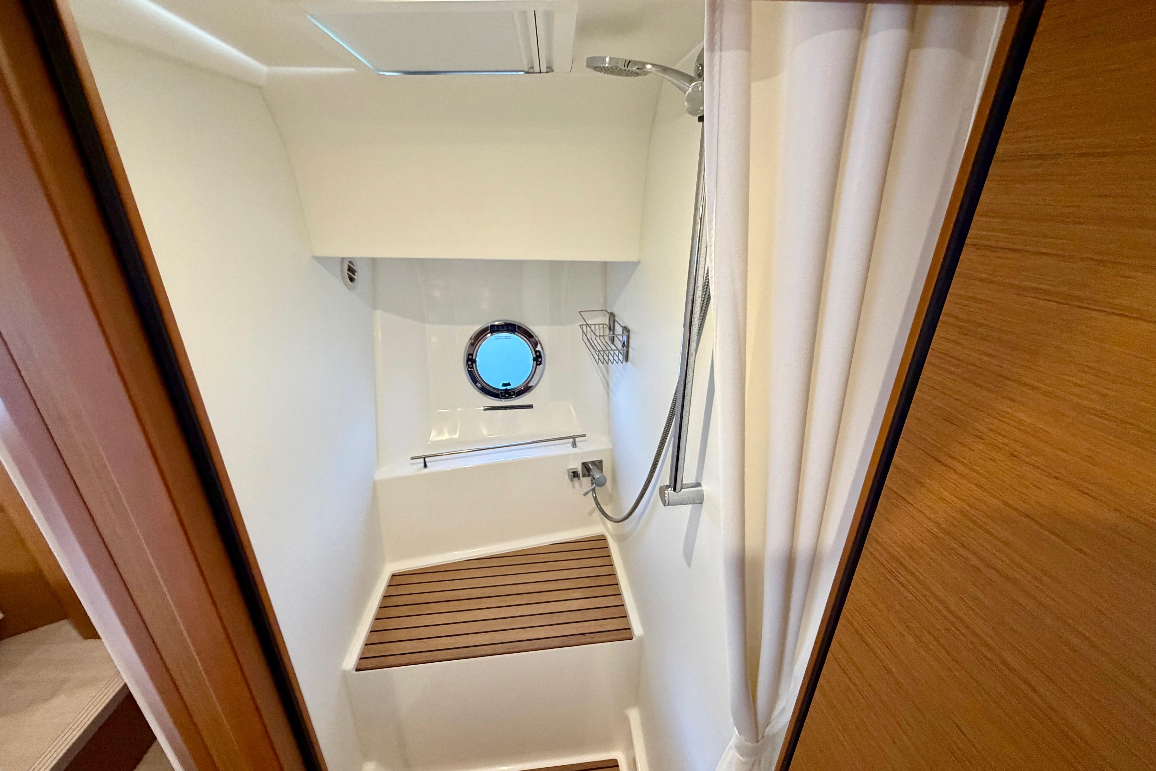 Shower area in 2025 Beneteau Swift Trawler 41 Fly, featuring wooden slats and porthole window.