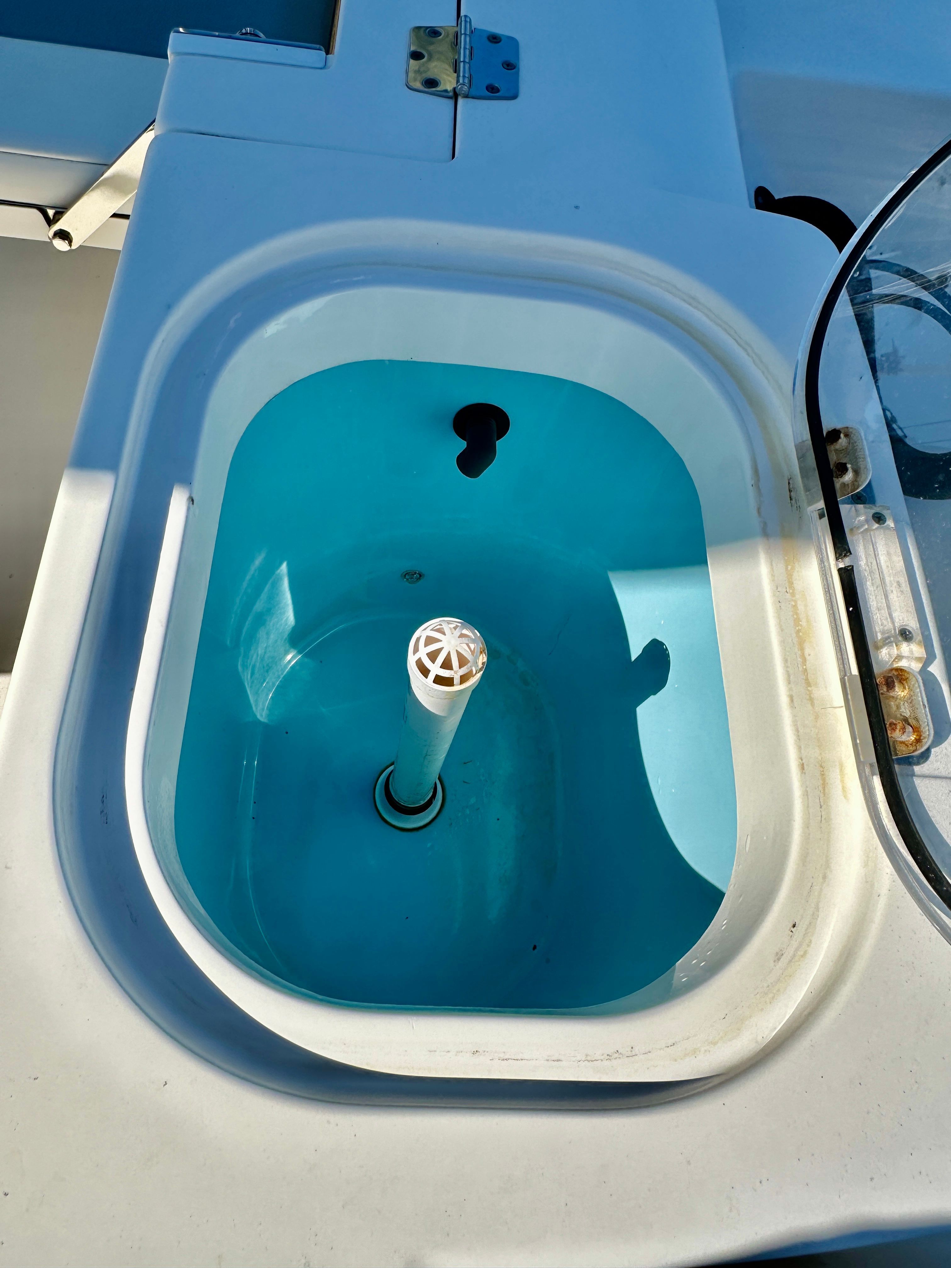 An oval, blue boat livewell with a white drain pipe in the center.