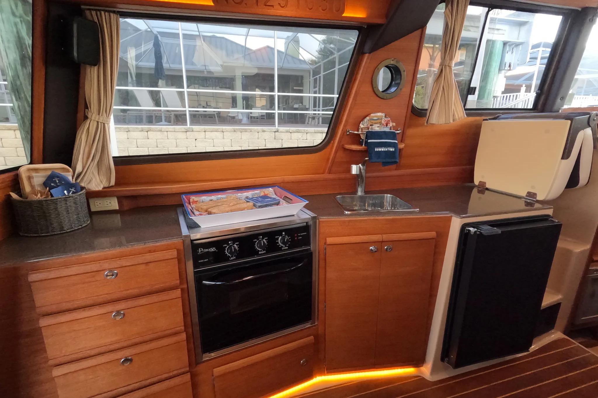 2015 Ranger Tugs R-29 S interior kitchen with wood cabinetry, oven, sink, and refrigerator.