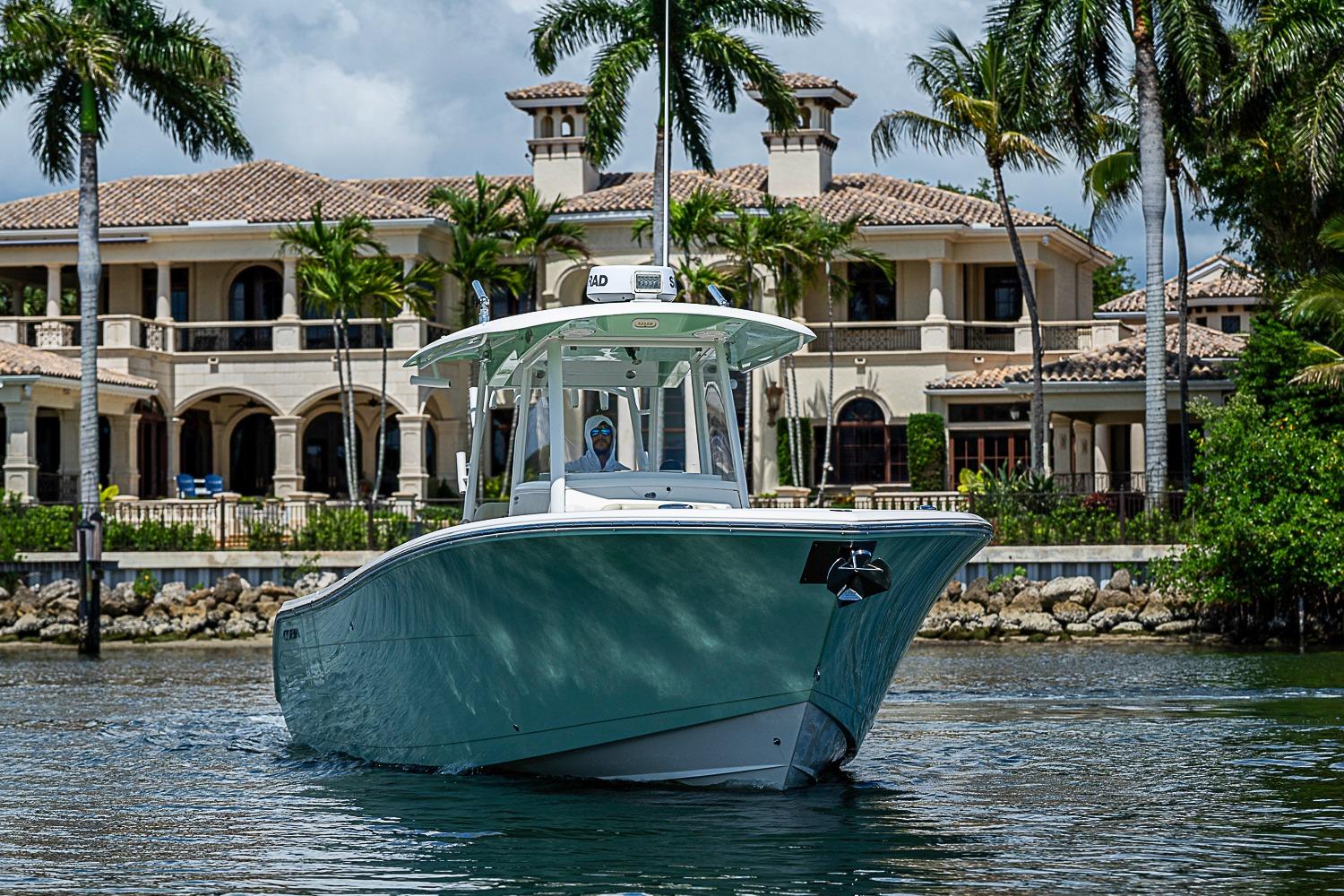 2019 Cobia 320 Center Console boat cruising near luxury waterfront mansion.