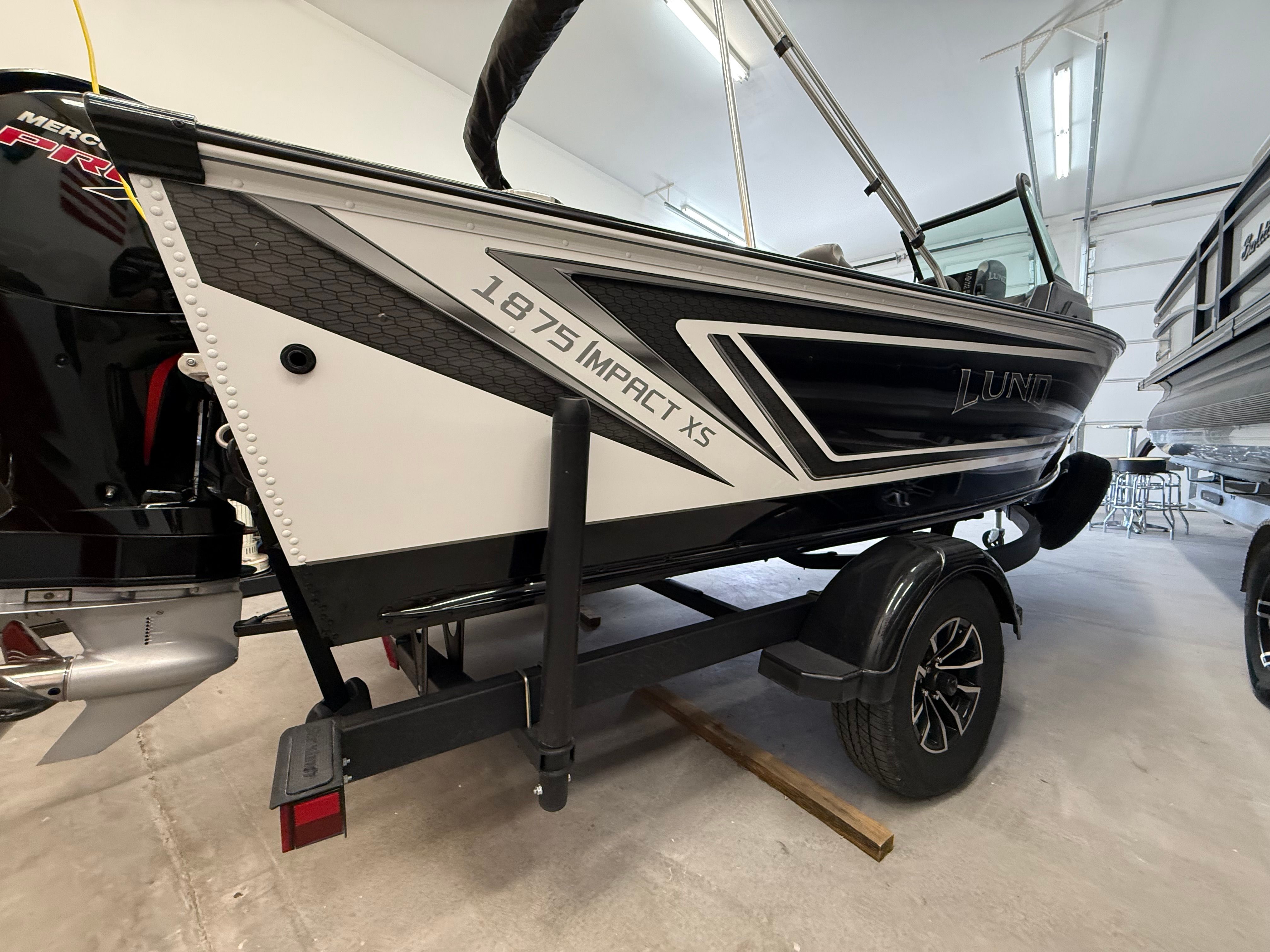 A 2025 Lund 1875 Impact XS Sport boat on a trailer in a showroom.