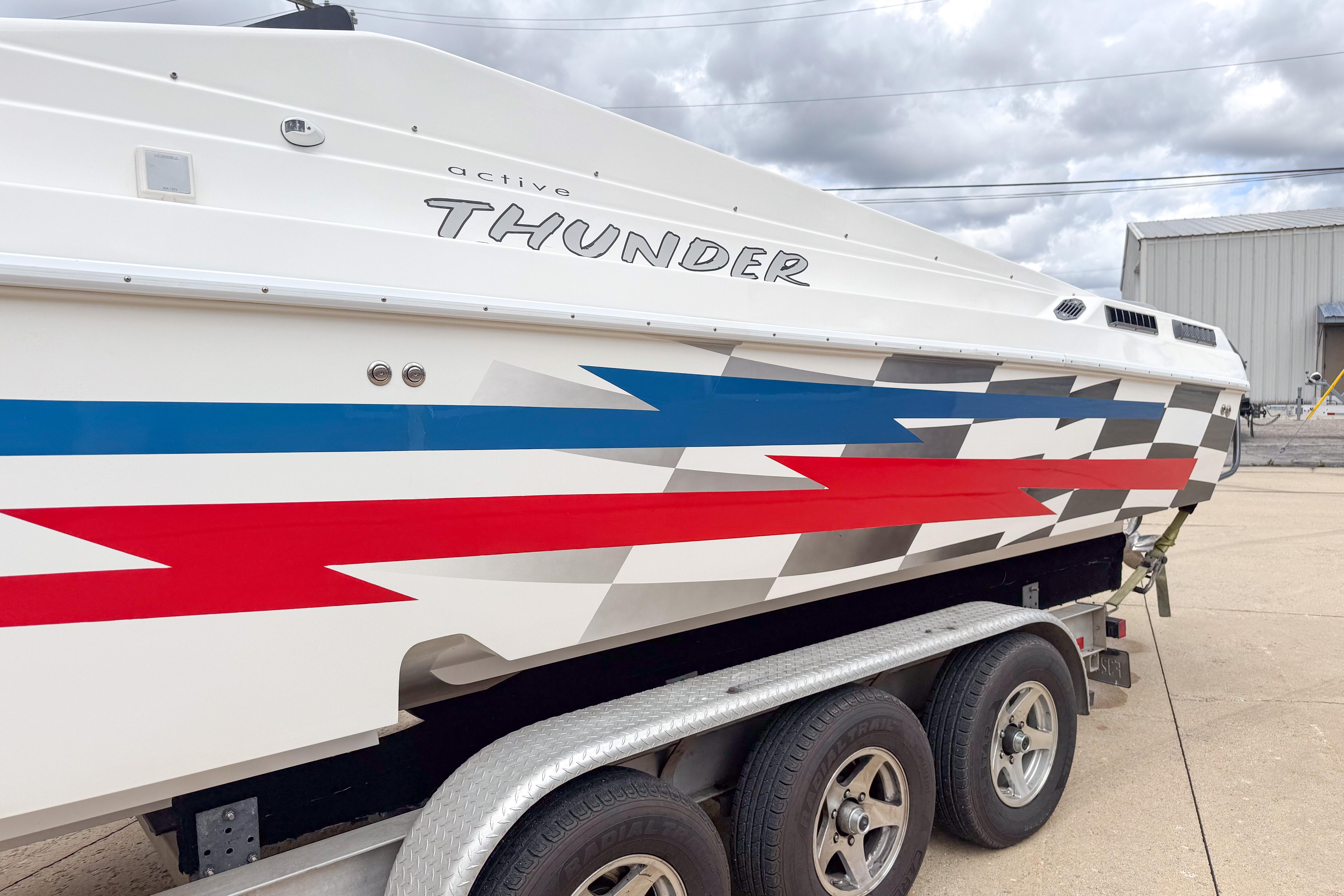 2002 Active Thunder 37 boat with vibrant red, blue, and gray graphics on a trailer.