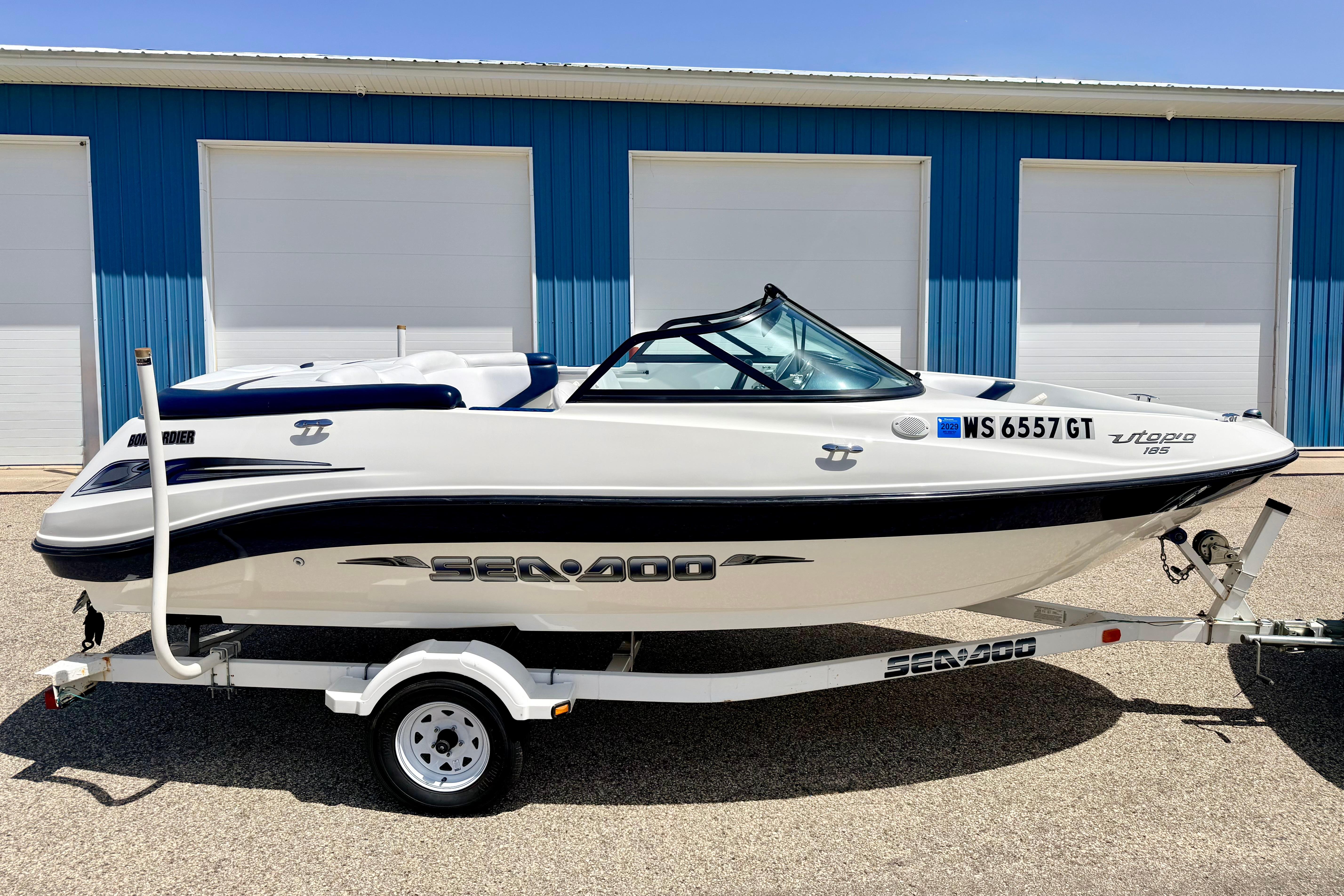 2004 Bombardier SEADOO Utopia 185 boat on trailer, parked near blue building.