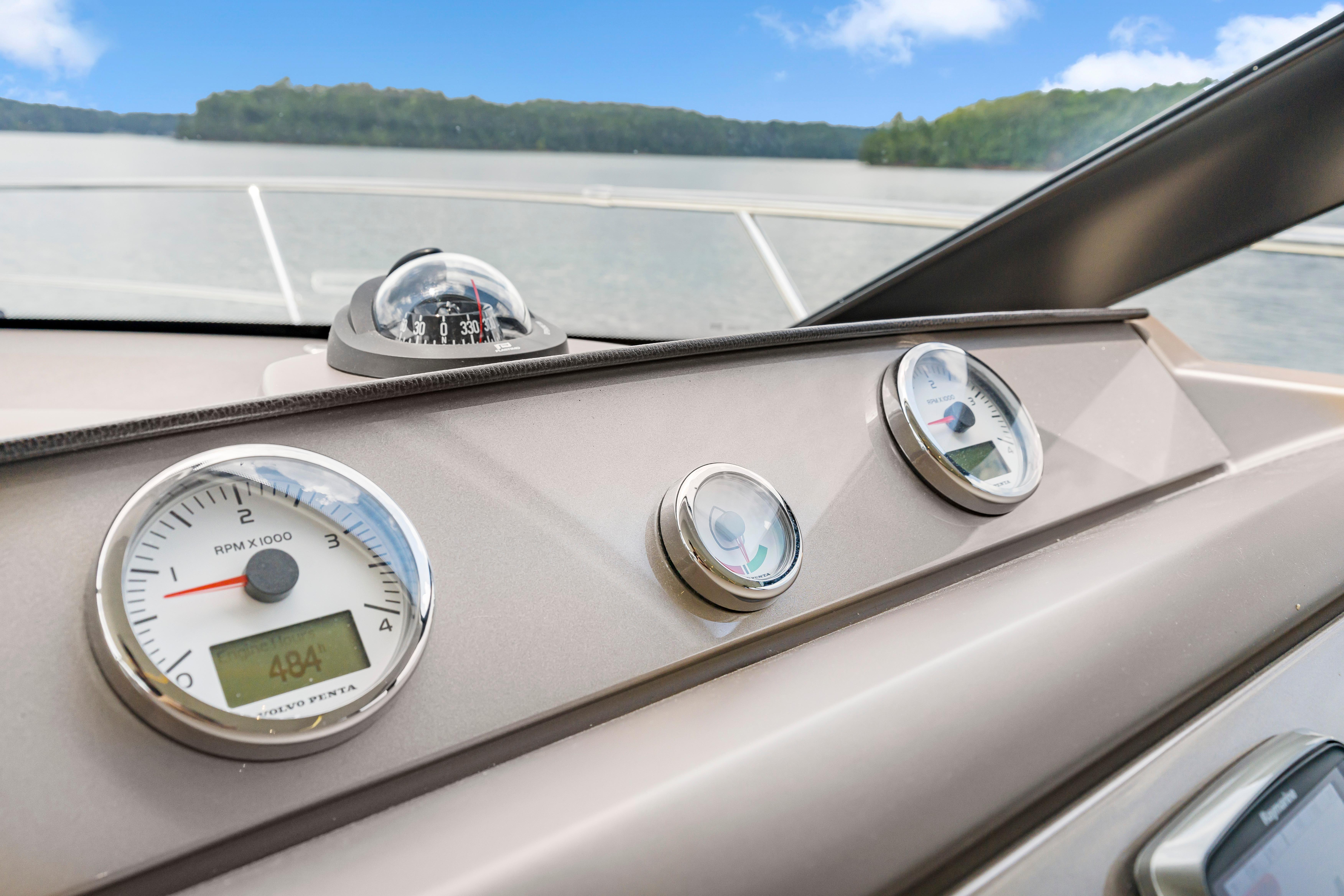 Control panel of a 2017 Prestige 500 yacht with gauges and compass, overlooking a serene lake.
