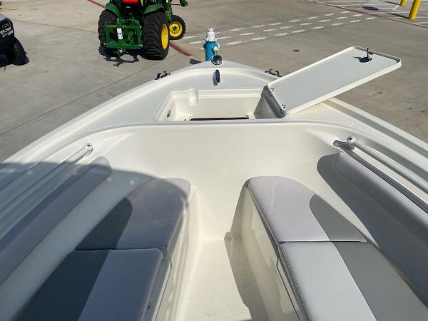 2024 Mako 214 CC boat interior with open storage compartment, docked near green tractor.
