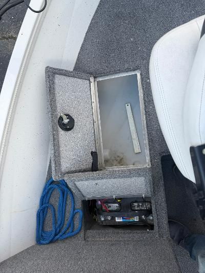 Open storage compartment on a boat with blue rope and battery.