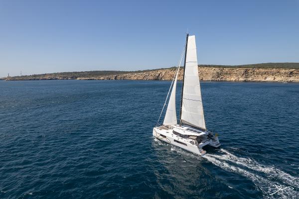 2025 Nautitech 44 Open catamaran sailing on open sea near rocky coastline.