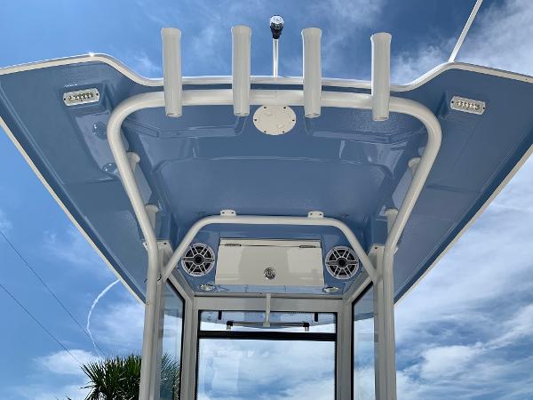 2024 Robalo 266 Cayman T-top with rod holders and speakers against a blue sky.