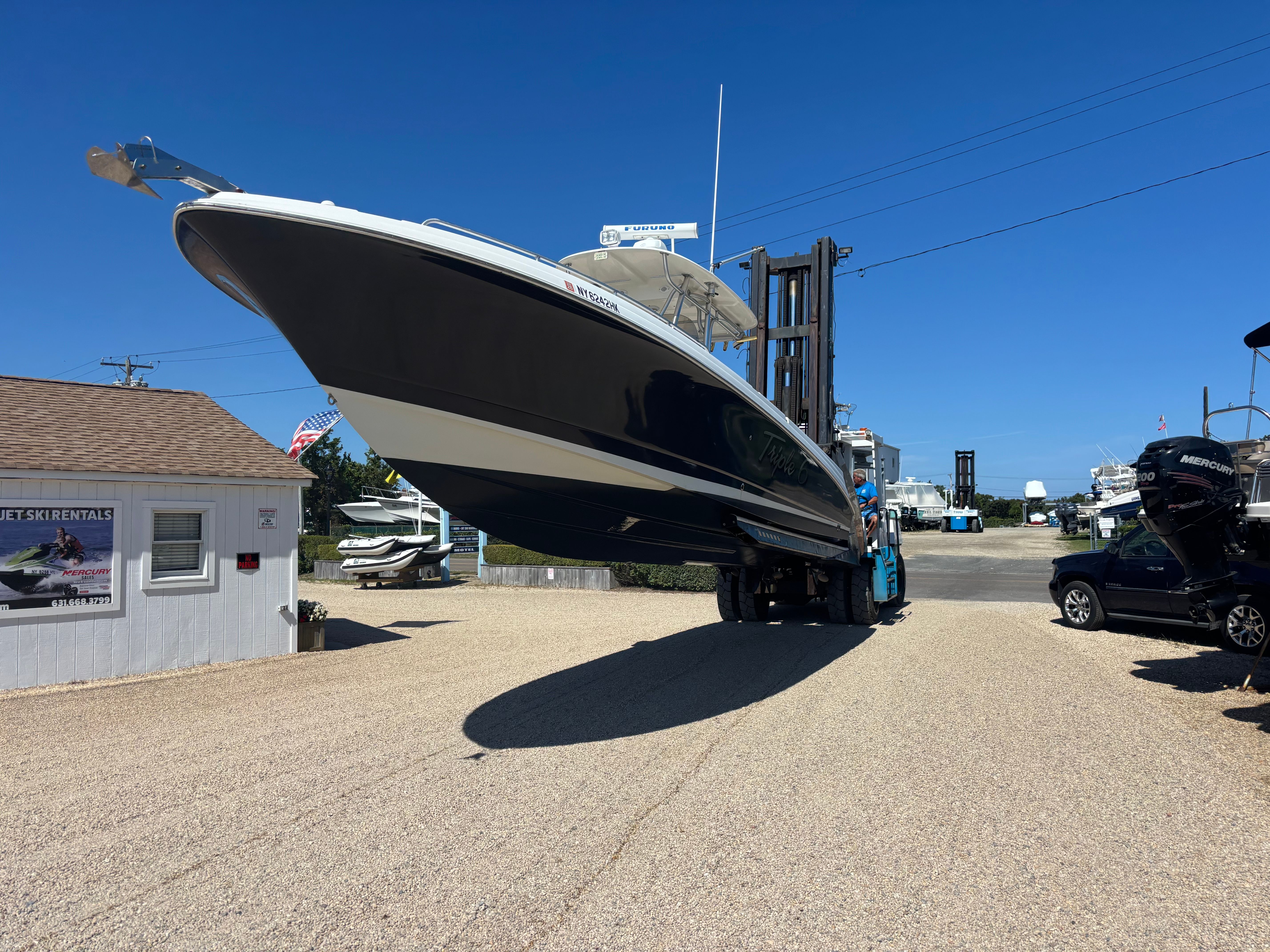 A 2006 Wellcraft Scarab 352 Sport being moved by a forklift on a gravel lot.