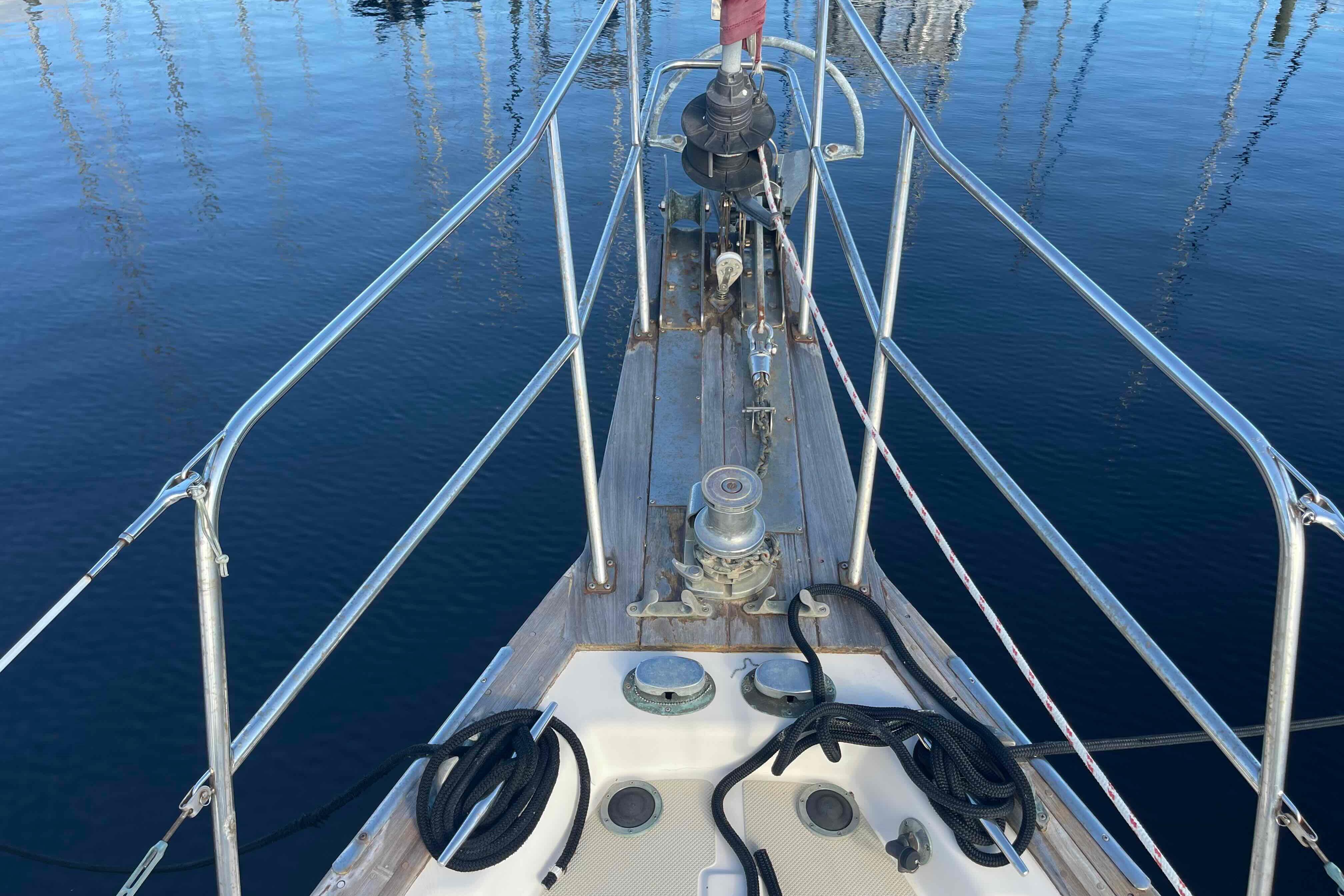 Bow of 1989 Island Packet 35 sailboat with ropes and winch, docked on calm water.