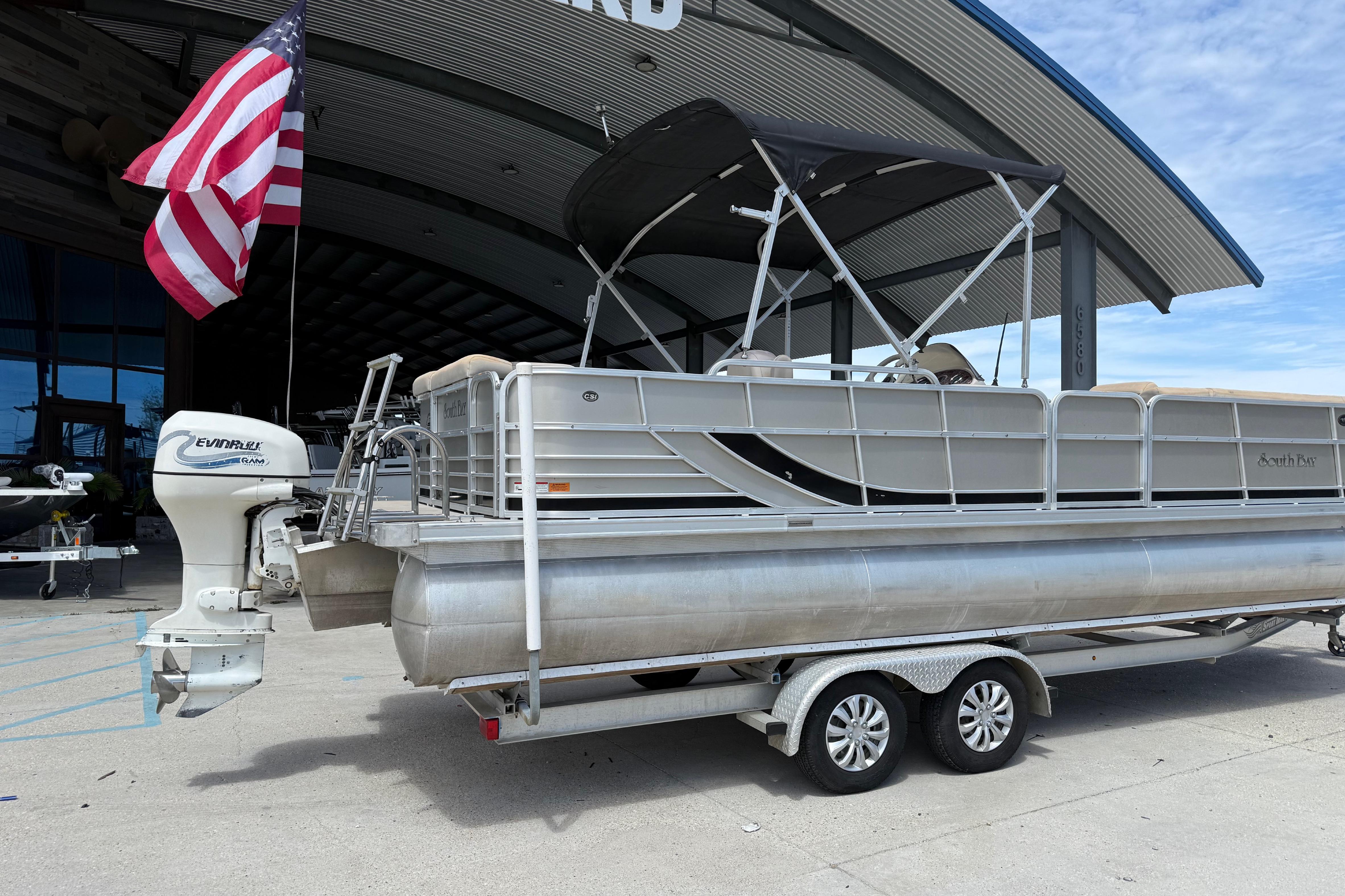 2012 South Bay 522 CR pontoon boat on trailer, parked near a building with an American flag.