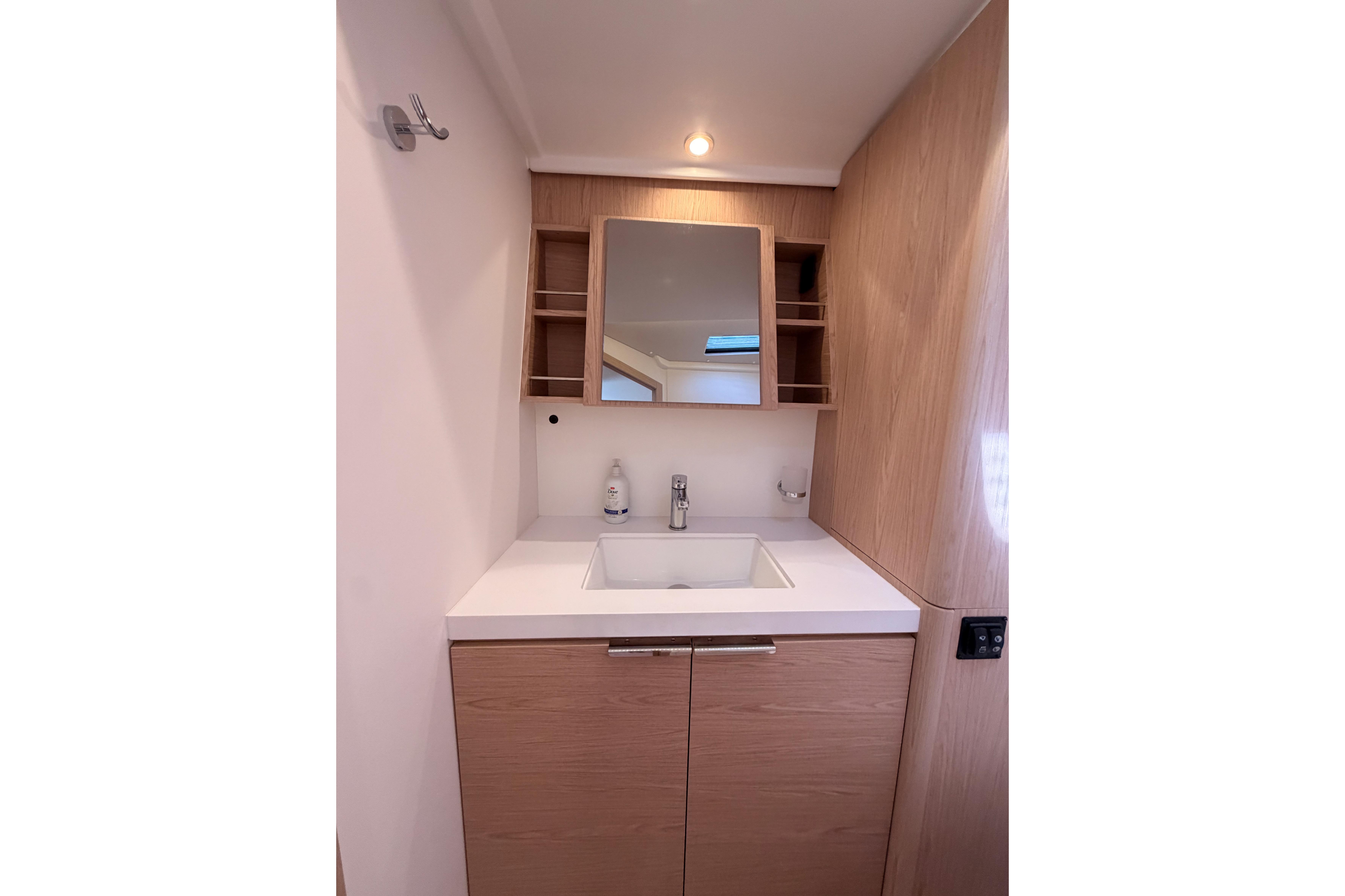 Modern bathroom vanity on 2022 Beneteau Oceanis Yacht 54, featuring sleek wood cabinetry and mirror.