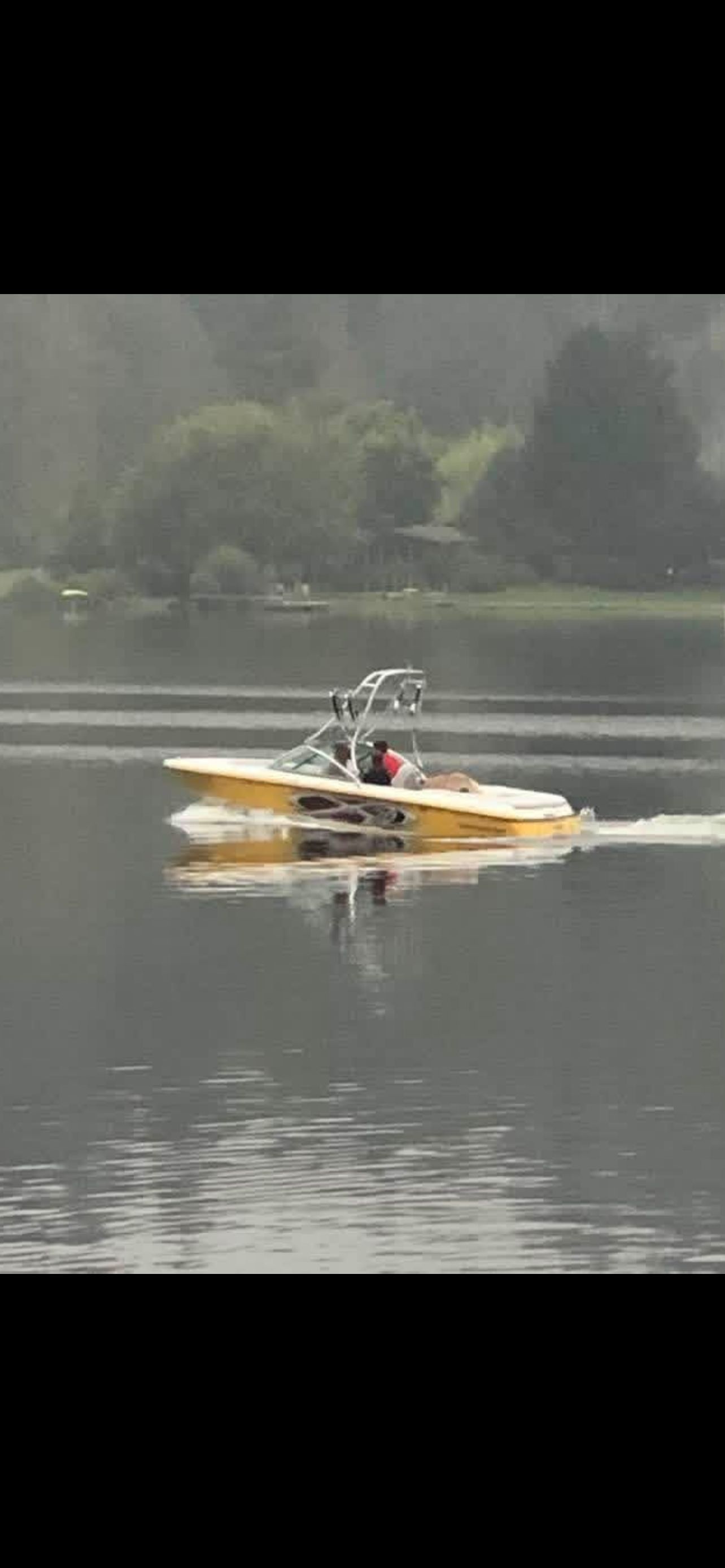 A yellow 2003 MasterCraft X2 boat cruising on a calm lake.