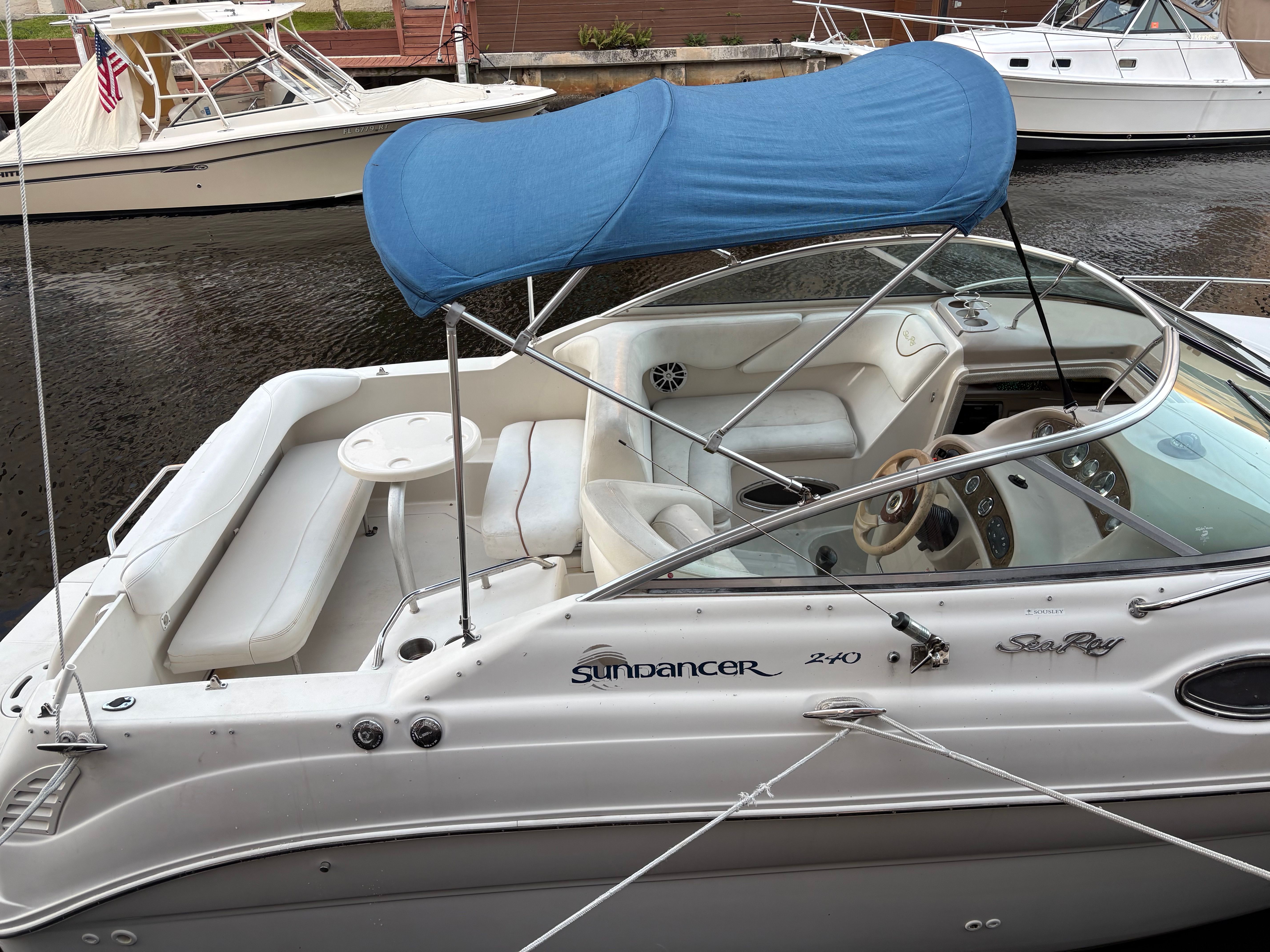 A 2001 Sea Ray 240 Sundancer with a blue sunshade, docked at a calm waterfront.