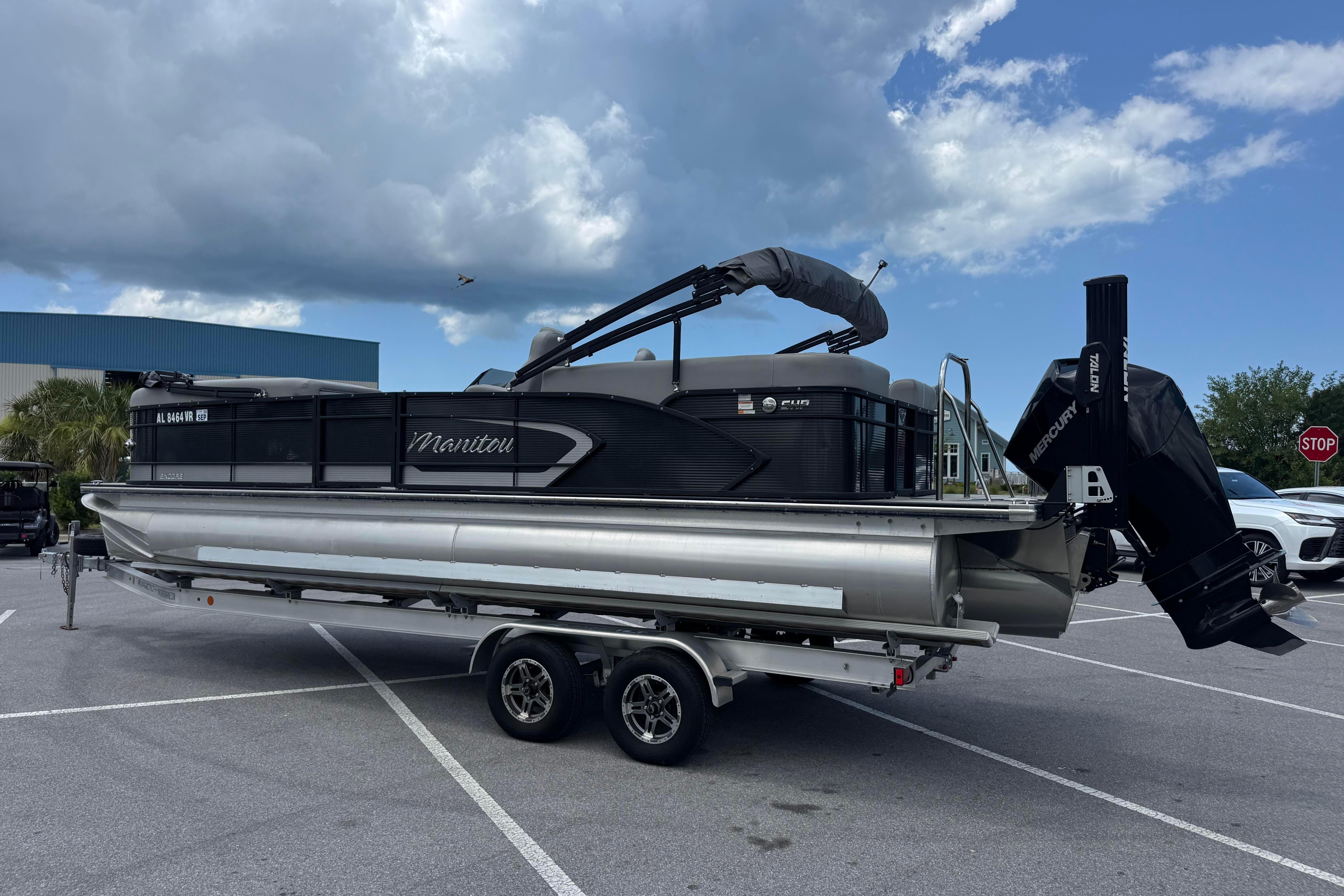 2022 Manitou 25 Encore pontoon boat on trailer under cloudy sky.