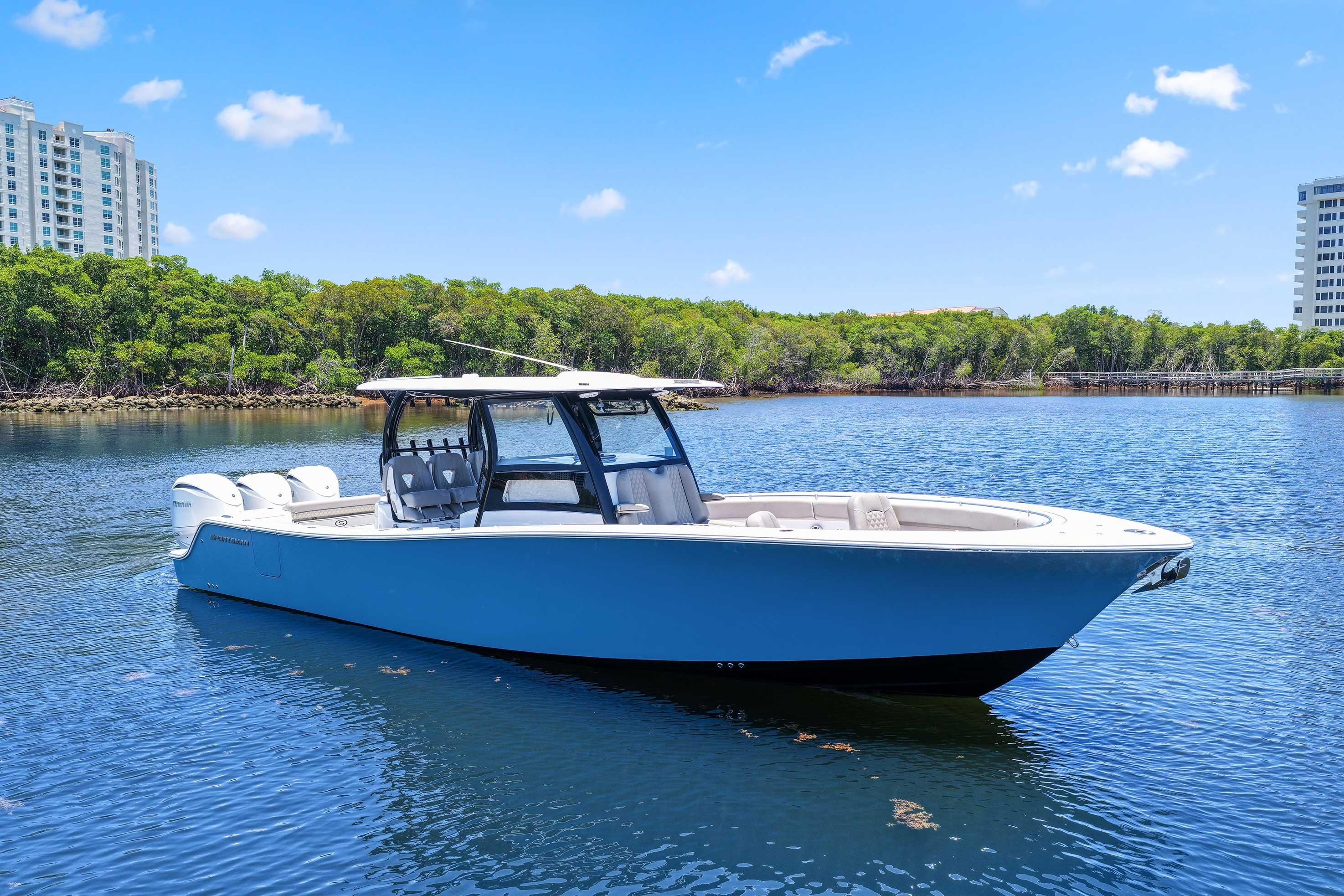 2024 Sportsman Open 352 Center Console boat on calm water, surrounded by greenery and buildings.