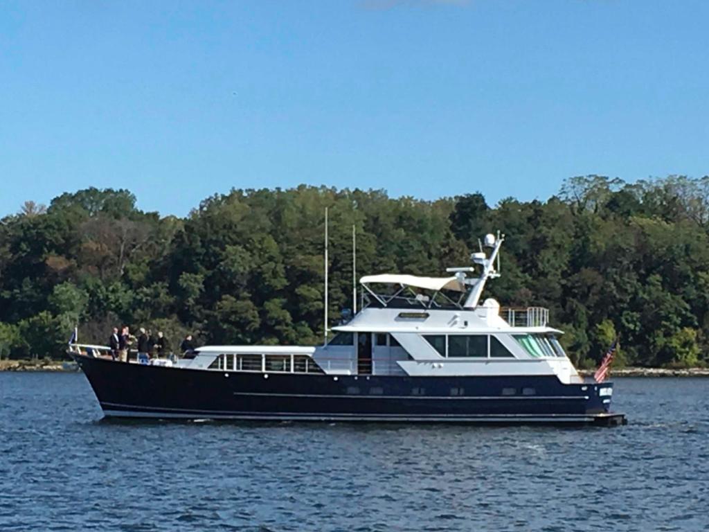 1982 Burger Flybridge yacht cruising on a serene lake with lush green trees in the background.