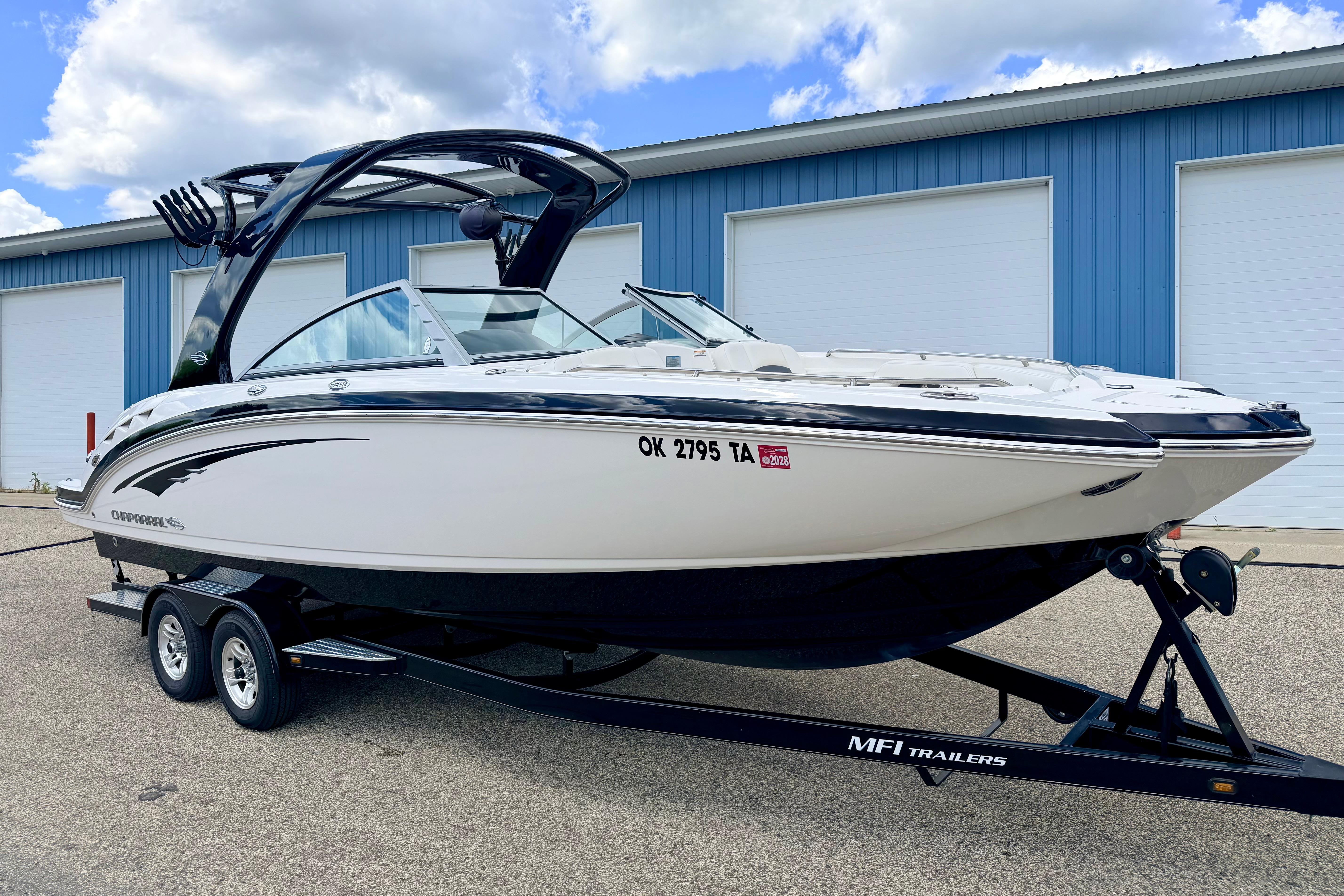 2015 Chaparral Sunesta 264 boat on trailer, parked near blue building under cloudy sky.