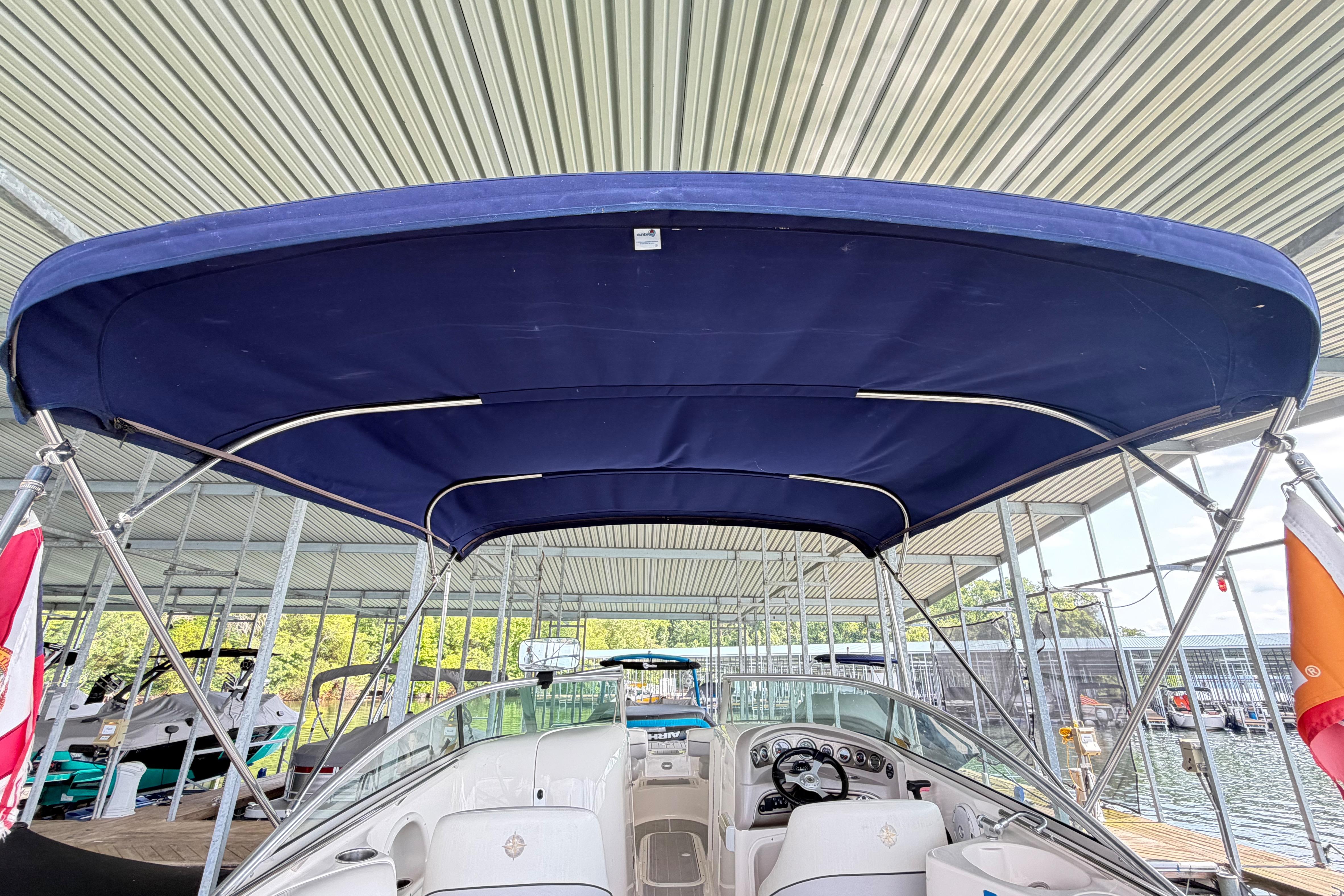 2010 Bryant 255 boat with blue canopy docked under a metal roof.