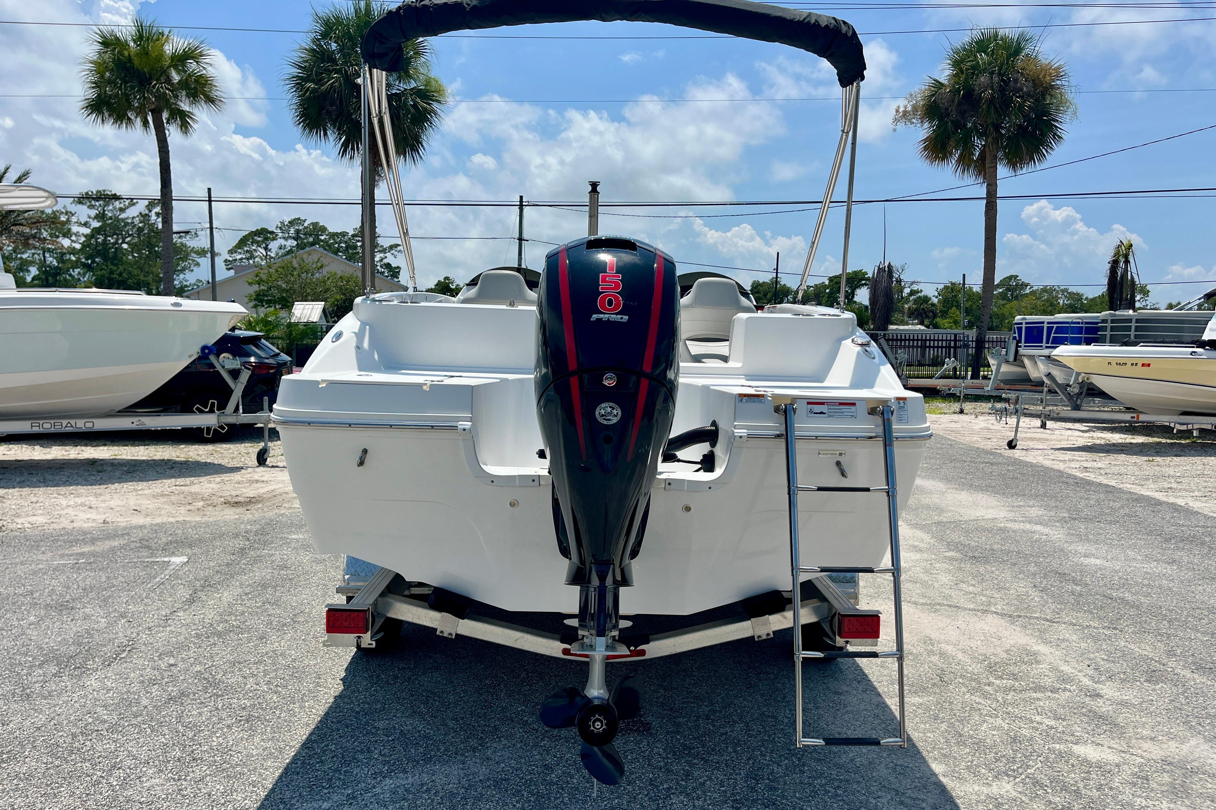 2024 Hurricane Sundeck Sport 218 OB boat with outboard motor and ladder, parked outdoors.