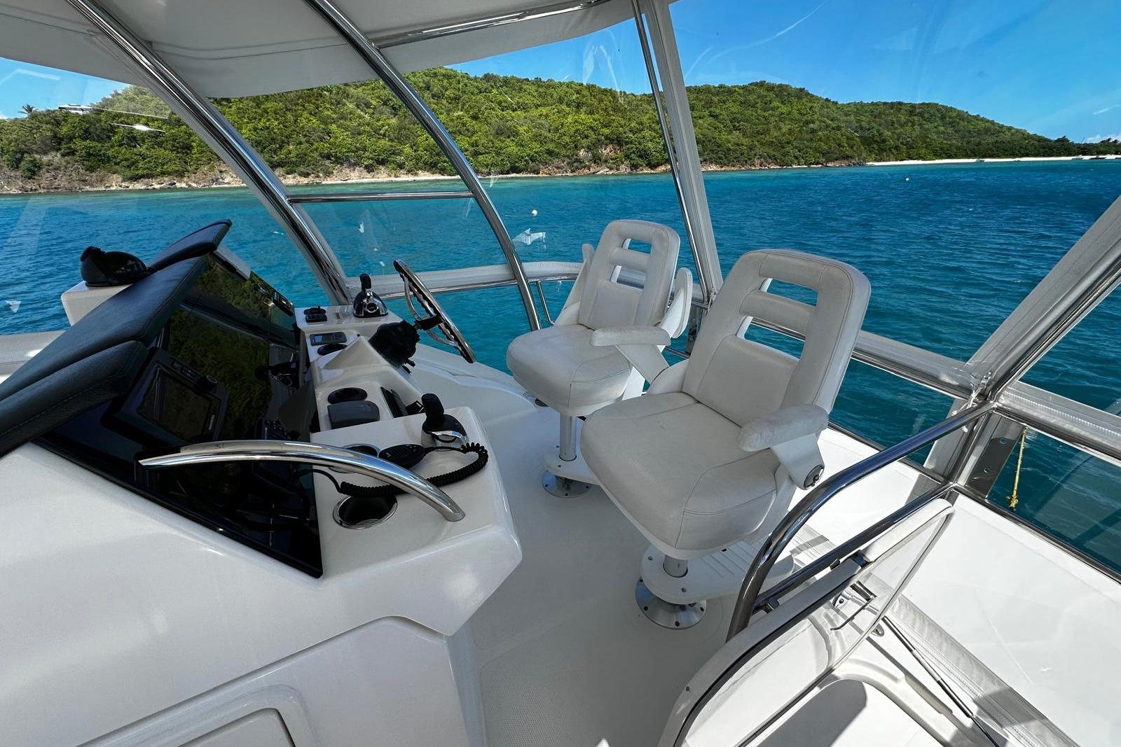 Flybridge of 2012 Riviera 43, featuring dual white captain chairs, overlooking serene blue waters.