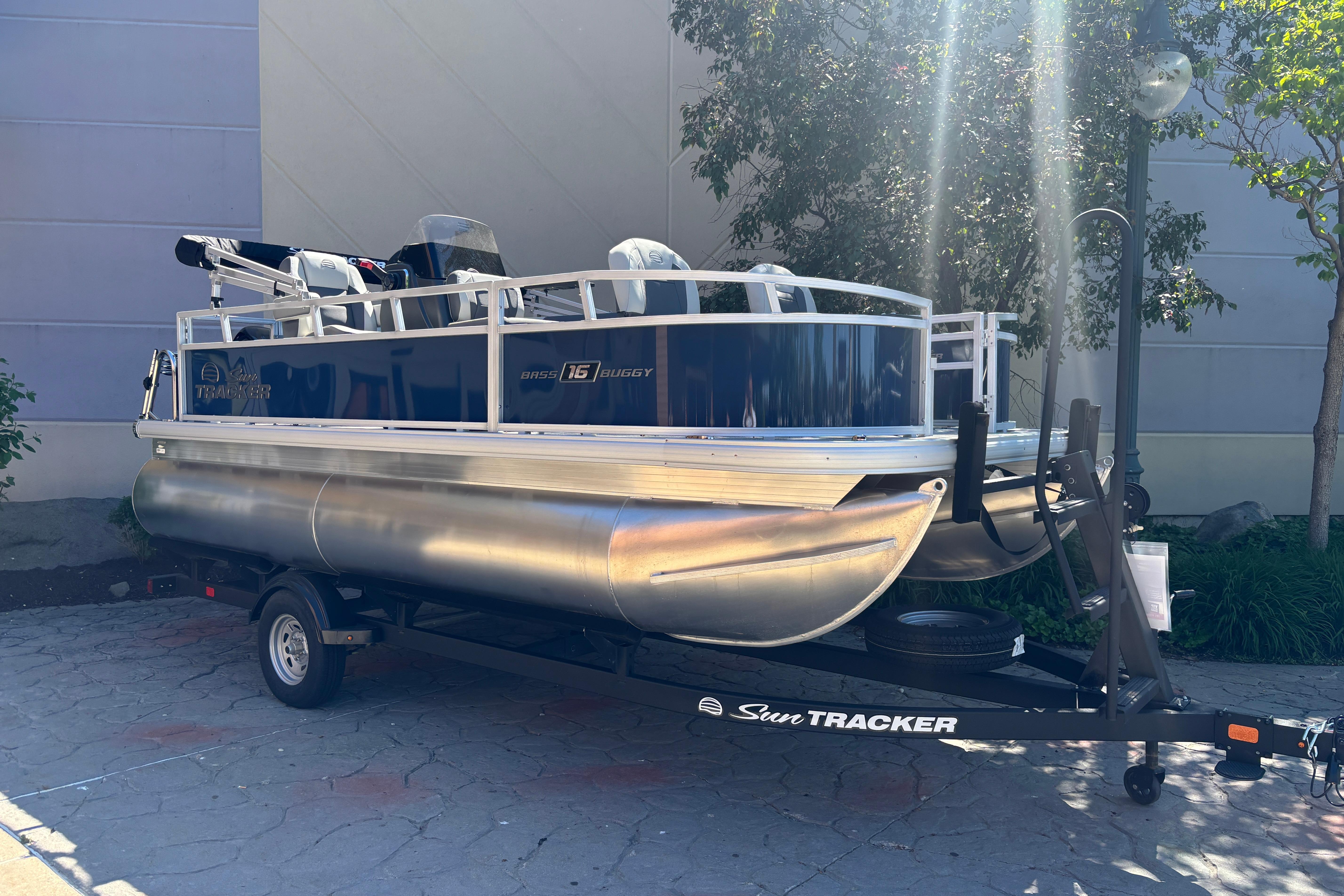 2026 Sun Tracker Bass Buggy 16 XL Select pontoon boat on trailer, parked outdoors.