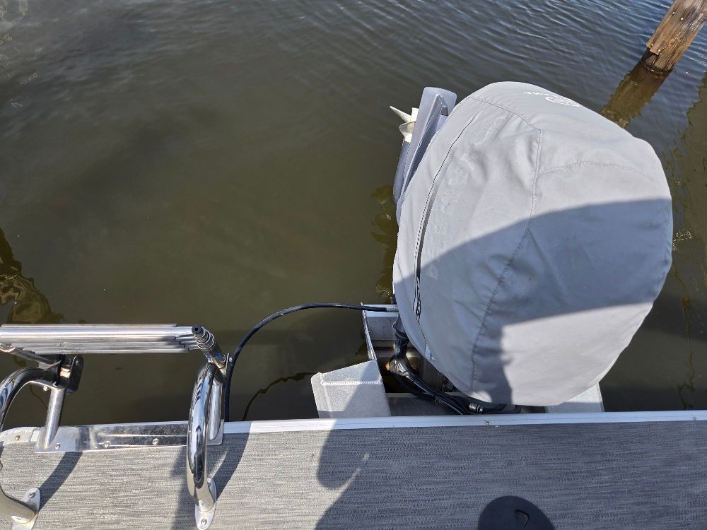 A covered outboard motor on a pontoon boat floating on the water.