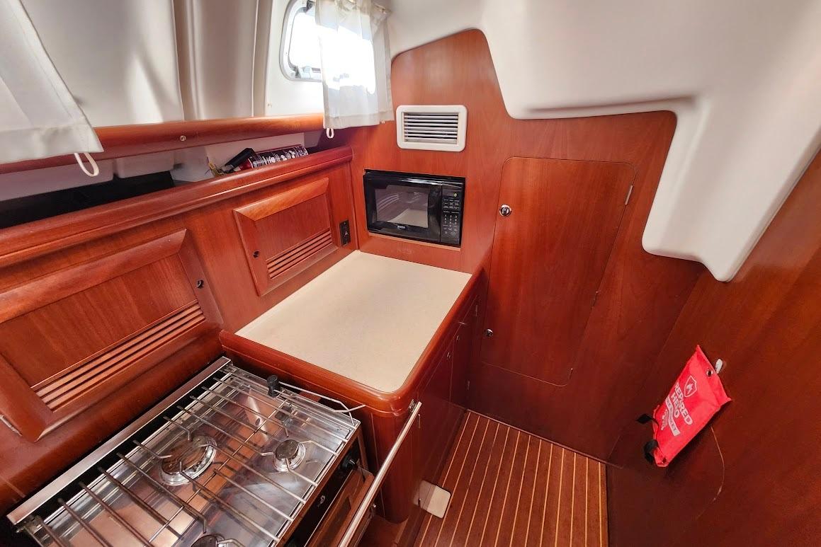 Interior of 2006 Beneteau 473 yacht kitchen with stove, microwave, and wooden cabinetry.