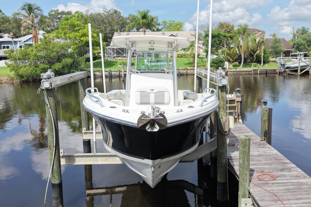 2018 Mako 284 Center Console boat docked on a lift by a scenic waterfront.
