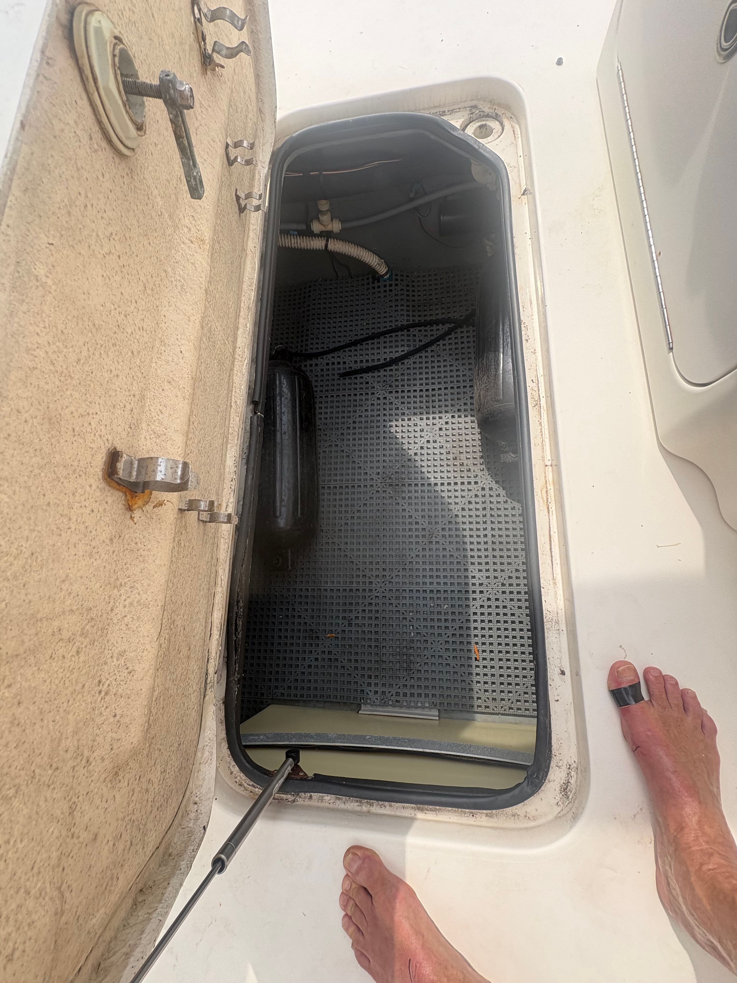 An open storage compartment on a boat with gray flooring and visible hinges.