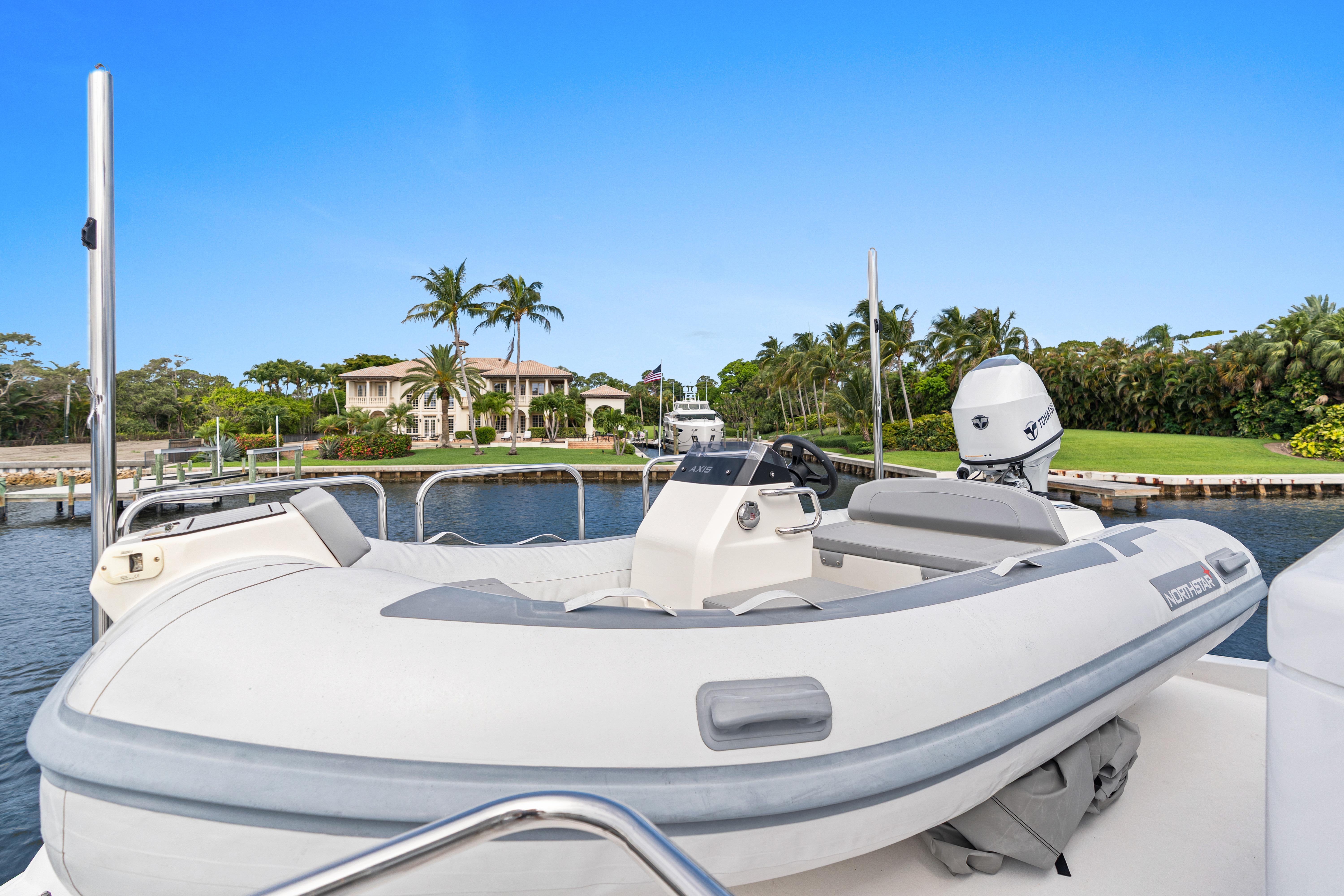 Luxury yacht with inflatable boat docked near waterfront mansion, clear blue sky. Hatteras 64 Motor Yacht 2008.