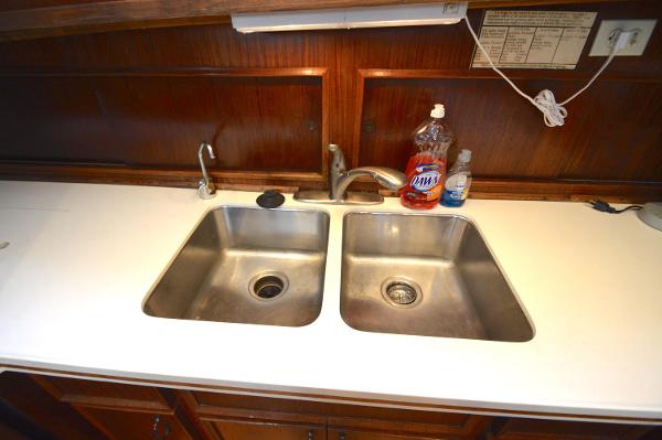 Stainless steel double sink in a yacht kitchen with wooden cabinets and cleaning supplies.