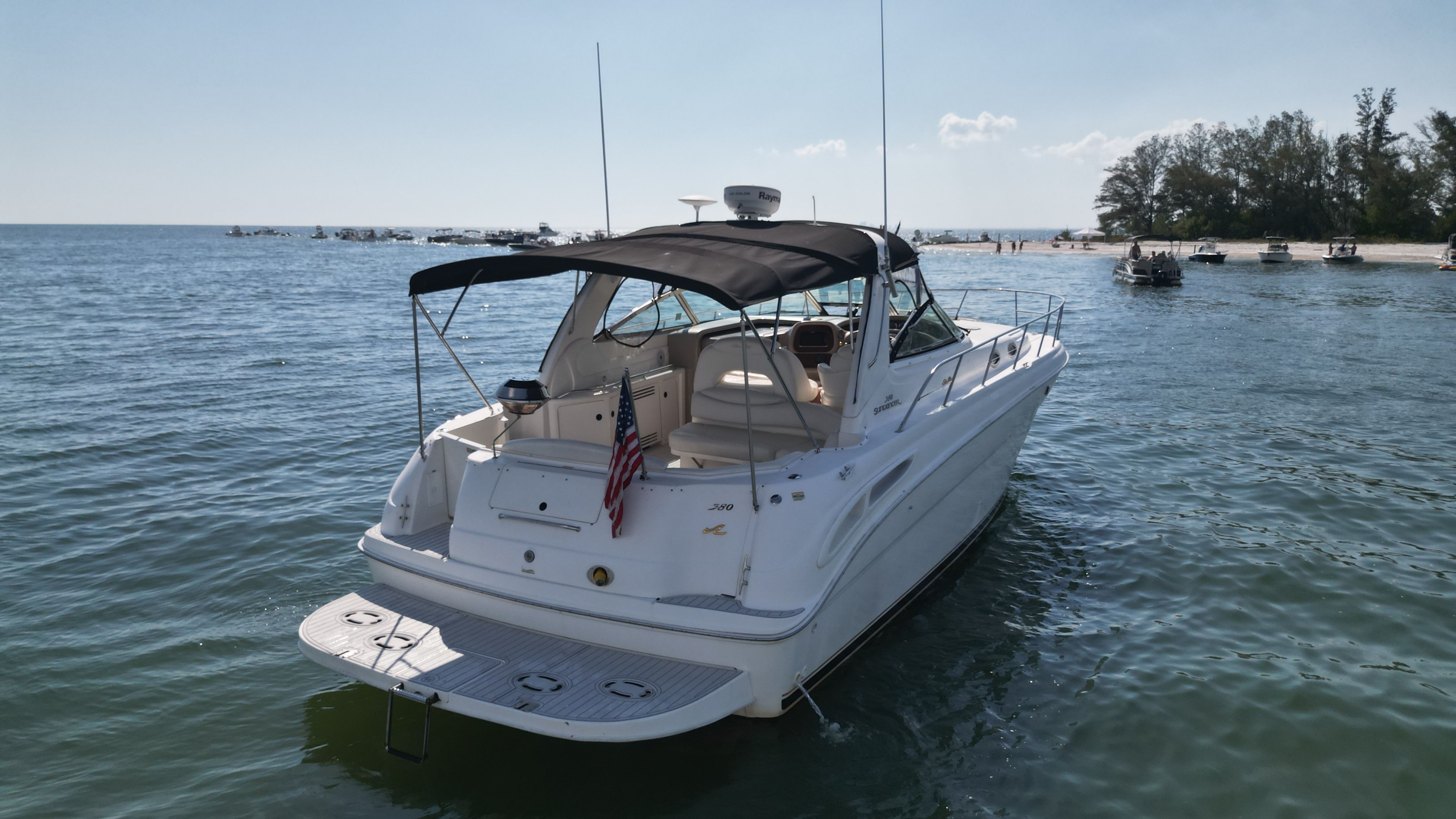 A white motorboat, Sea Ray 380 Sundancer, is on calm water near a beach.