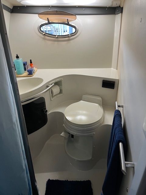 The image shows a boat bathroom with a toilet, sink, and porthole.