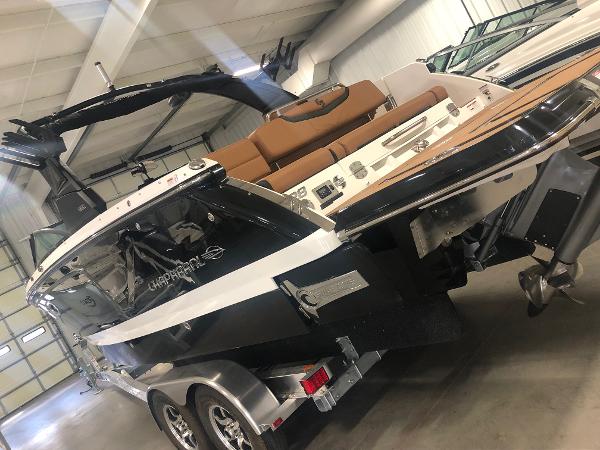 2024 Chaparral 28 Surf boat in showroom, featuring sleek design and dual-axle trailer.