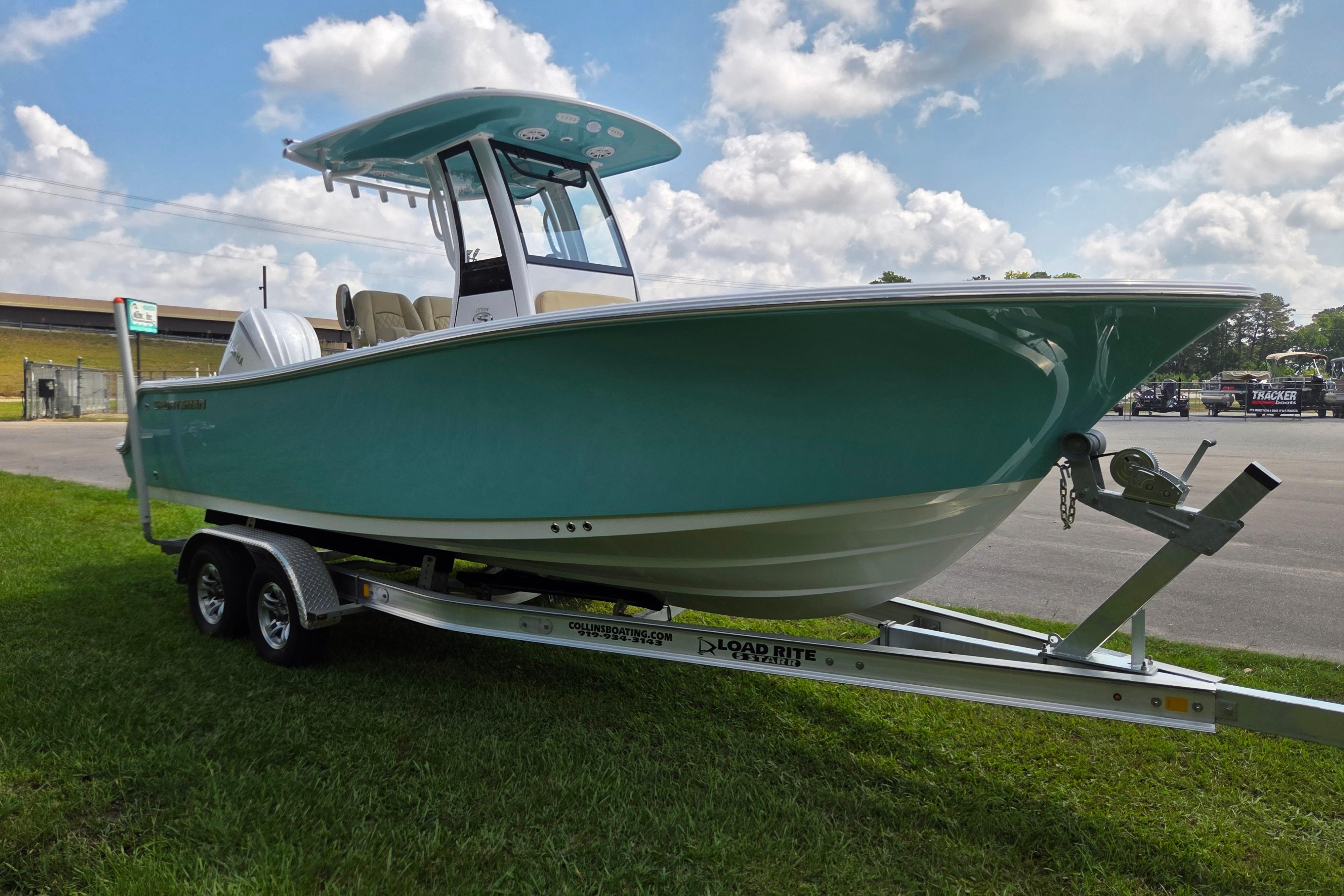 2026 Sportsman Open 232 Center Console boat on trailer, parked on grass under cloudy sky.