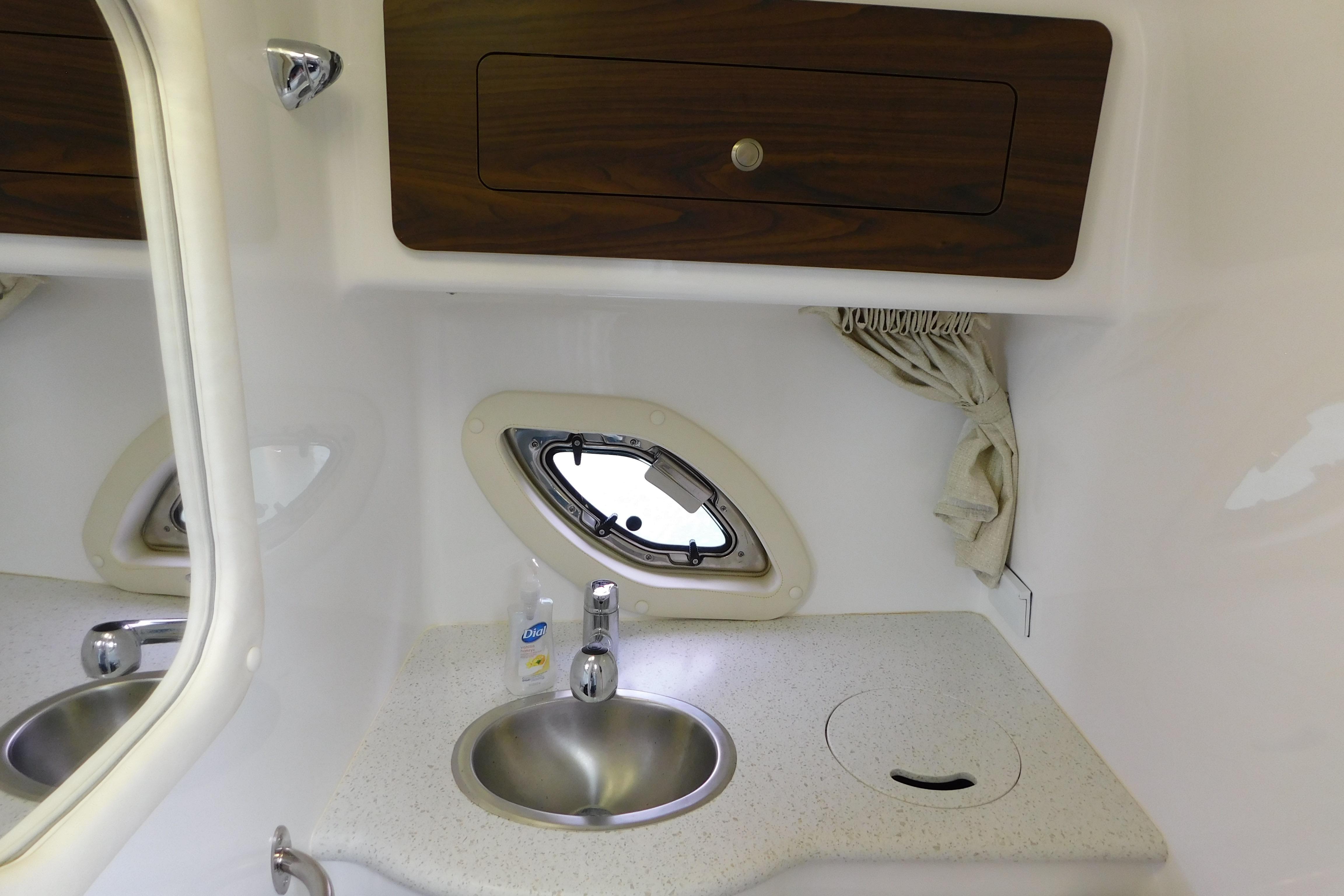 2017 Rinker EX 320 boat interior with sink, porthole, and wooden cabinet.