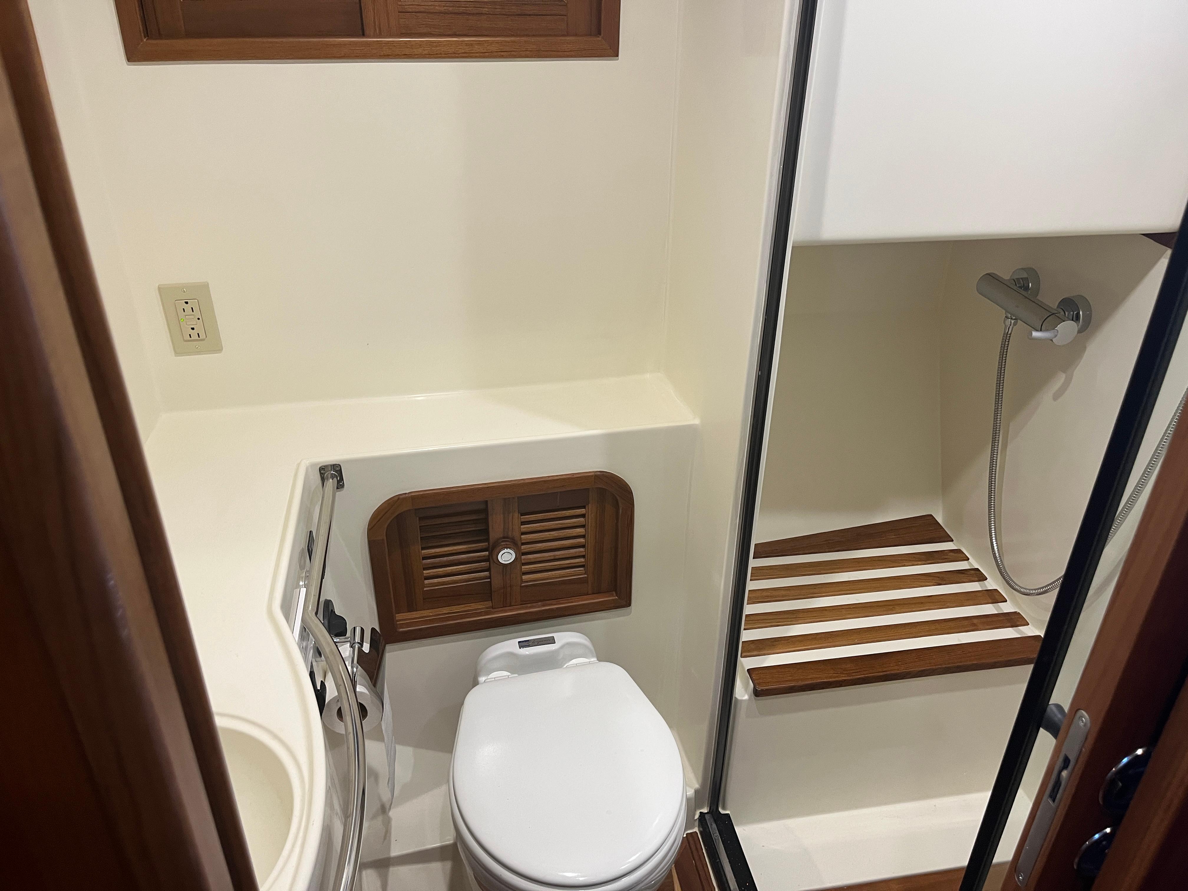 2025 Helmsman Trawlers 43E PILOTHOUSE bathroom with shower, toilet, and wooden accents.