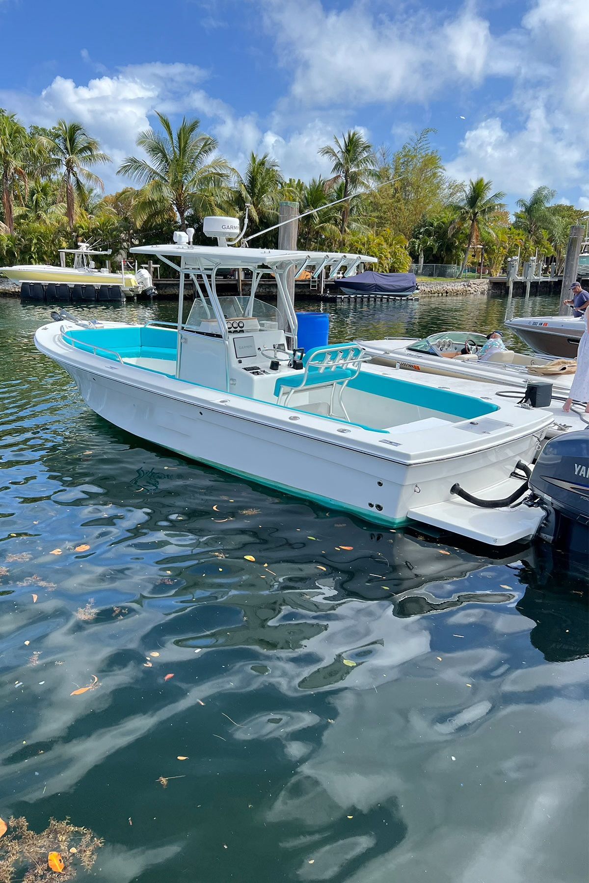 A white boat with turquoise interior sits on a calm, palm-lined waterway.