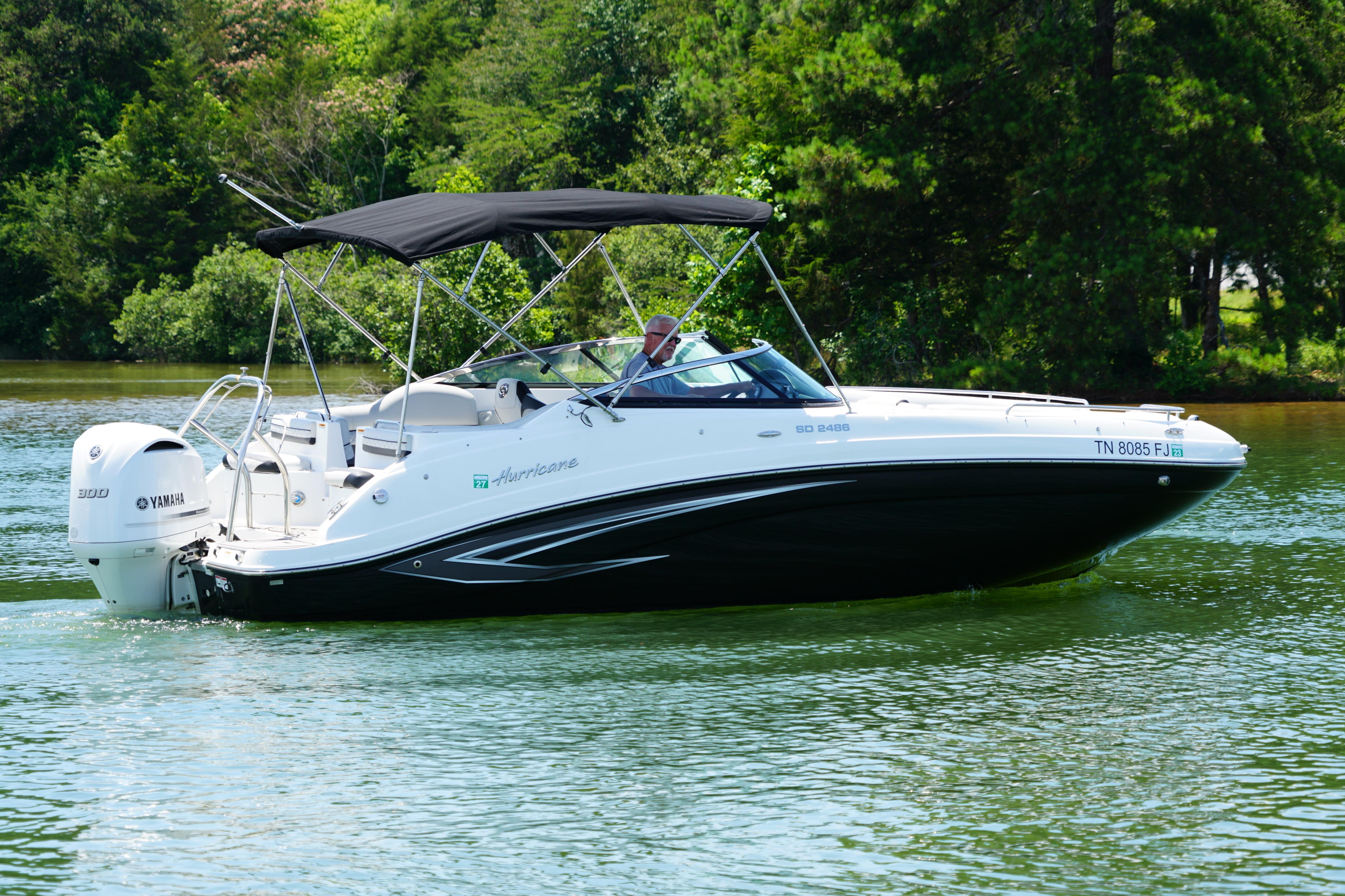 2020 Hurricane SunDeck 2486 OB boat cruising on a serene lake with lush greenery.
