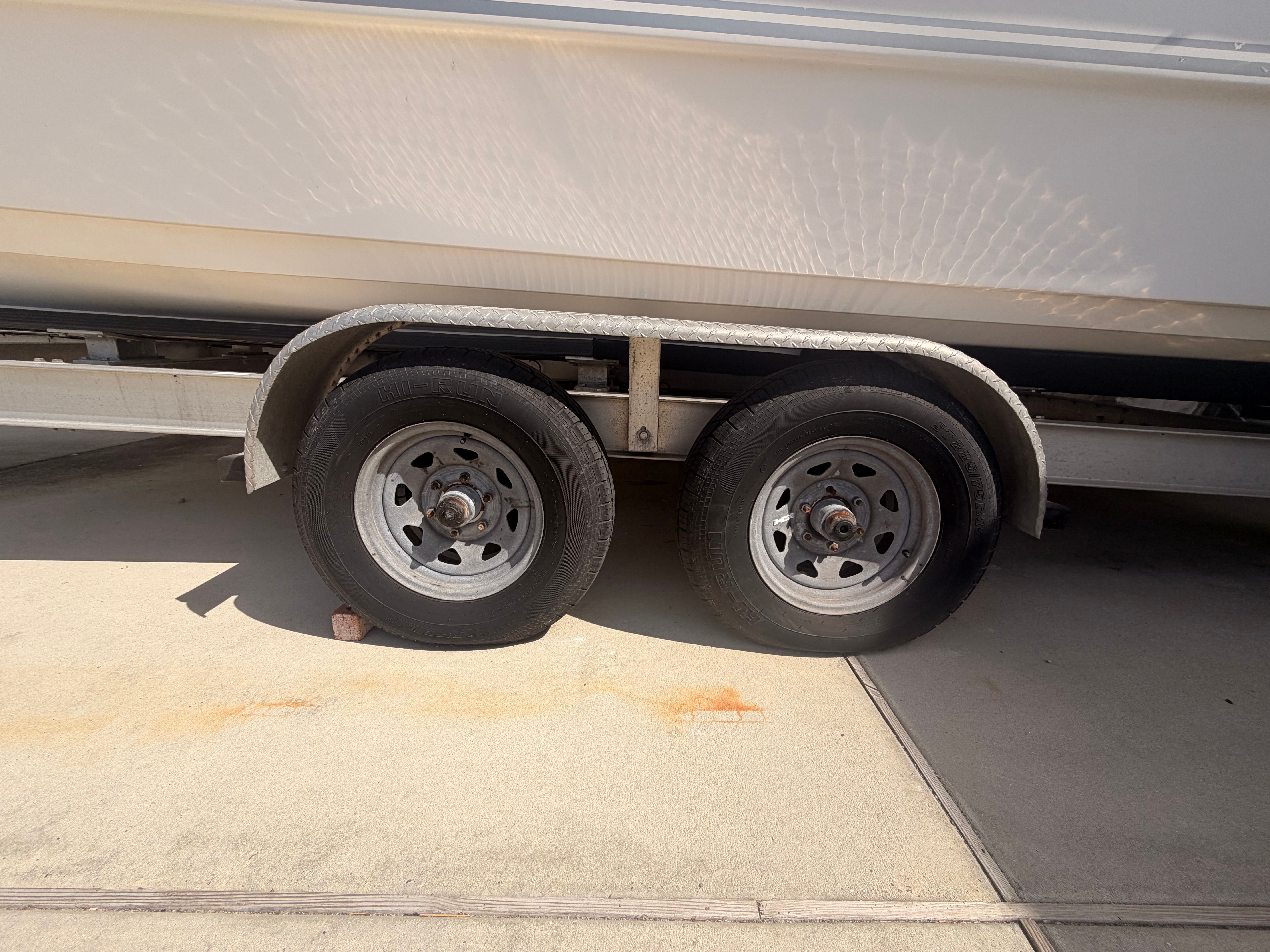 A boat on a trailer with two wheels, parked on a concrete surface.